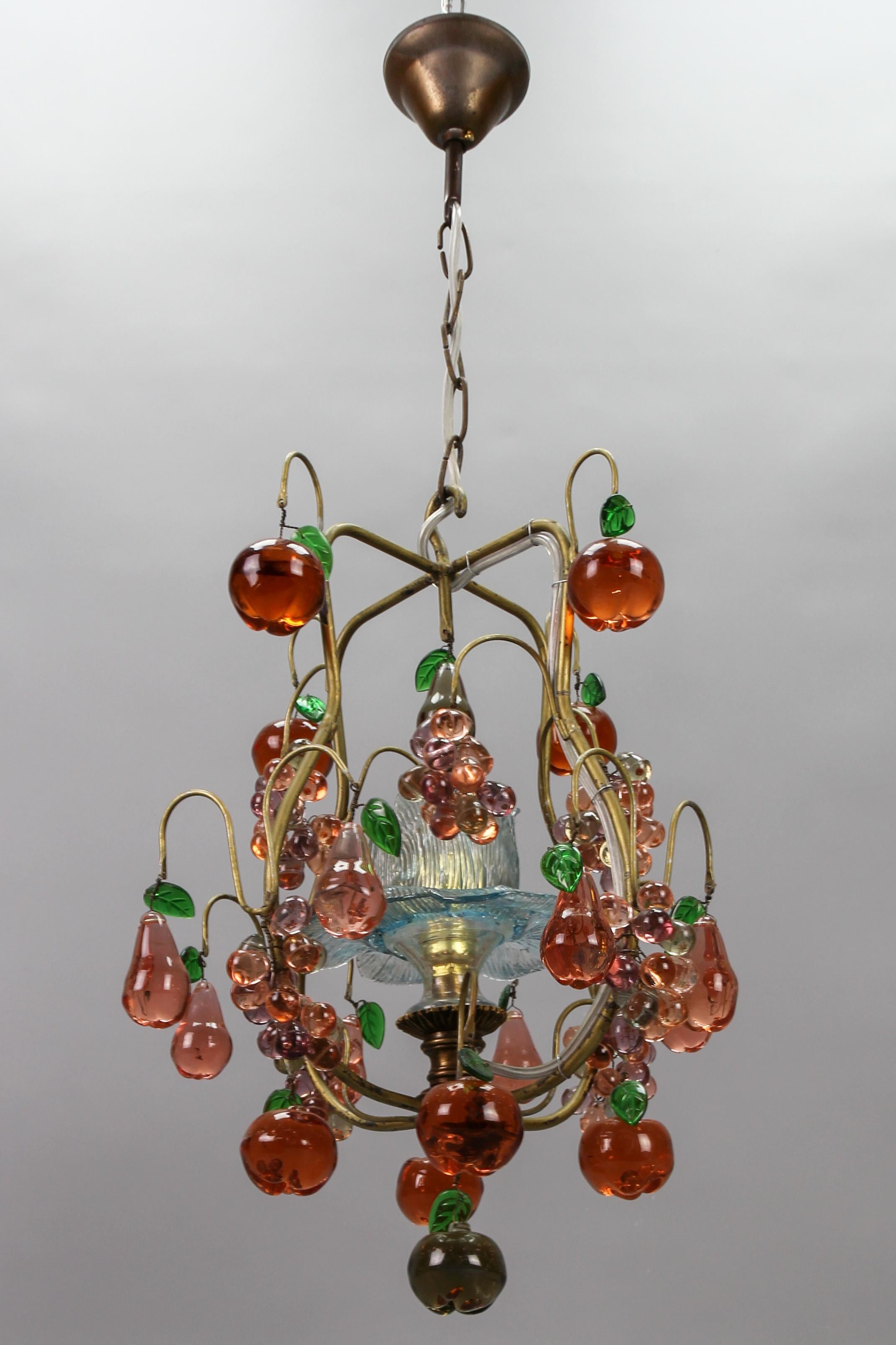 Italian Venetian single-light pendant chandelier with multicolored Murano glass fruits and berries from the circa 1950s.
This adorable and compact size Italian Hollywood Regency-style pendant chandelier features a golden-colored metal frame adorned