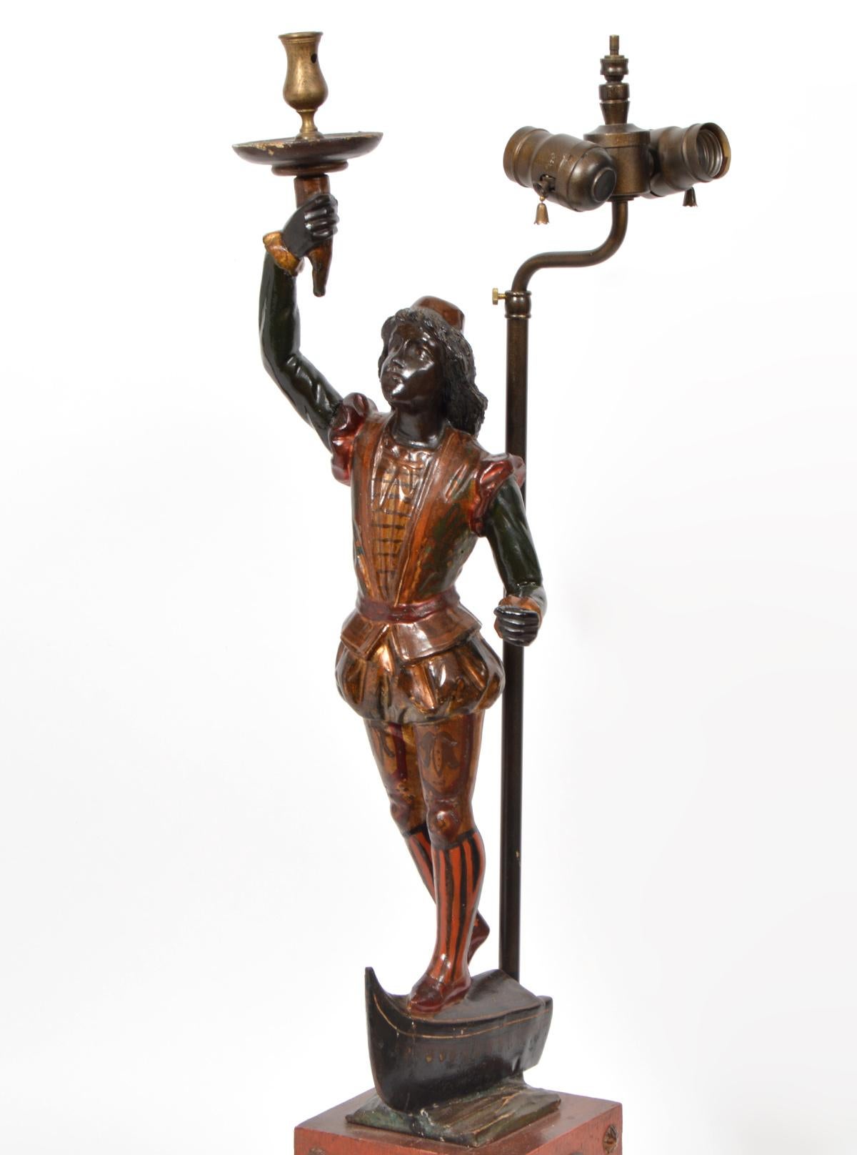 This Italian Venetian style table lamp features a young waiter wearing renaissance style costume standing on a partial gondola raising his right arm with a tray and holding a ceremonial pole in his left hand, early 20th century. The figure,