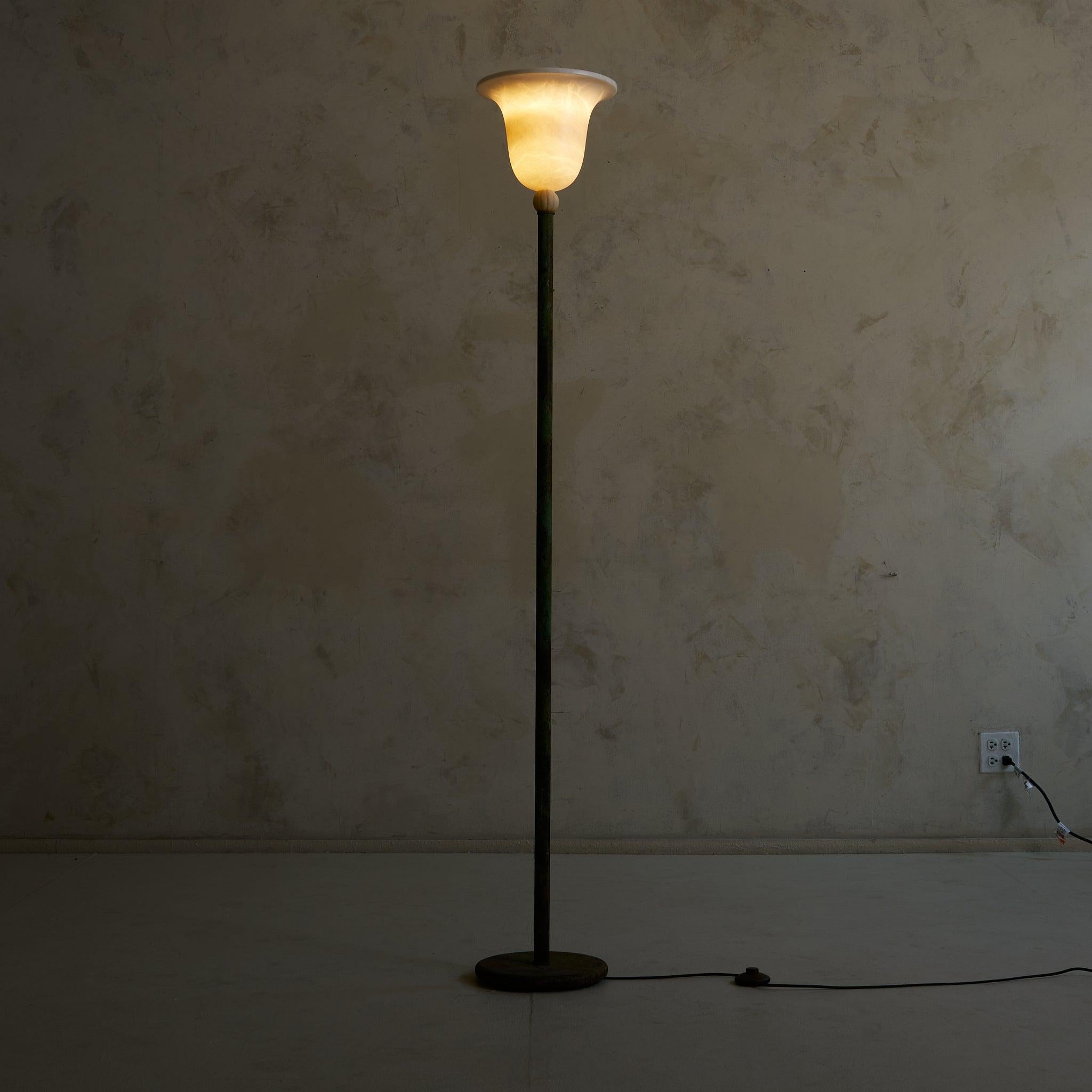 Ce lampadaire italien, datant des années 1940, se définit par son élégante patine usée par le temps. Une fine tige vert-de-gris s'élève d'une base circulaire lestée, culminant dans un abat-jour torchère en verre évasé. Le contraste entre le métal