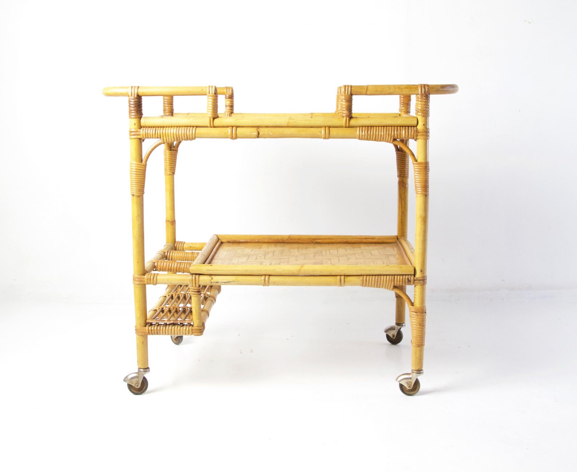 A vintage bar cart in bamboo, rattan and banana leaf with two tiers and space to hold three bottles. Has the original castors and is in overall great condition.