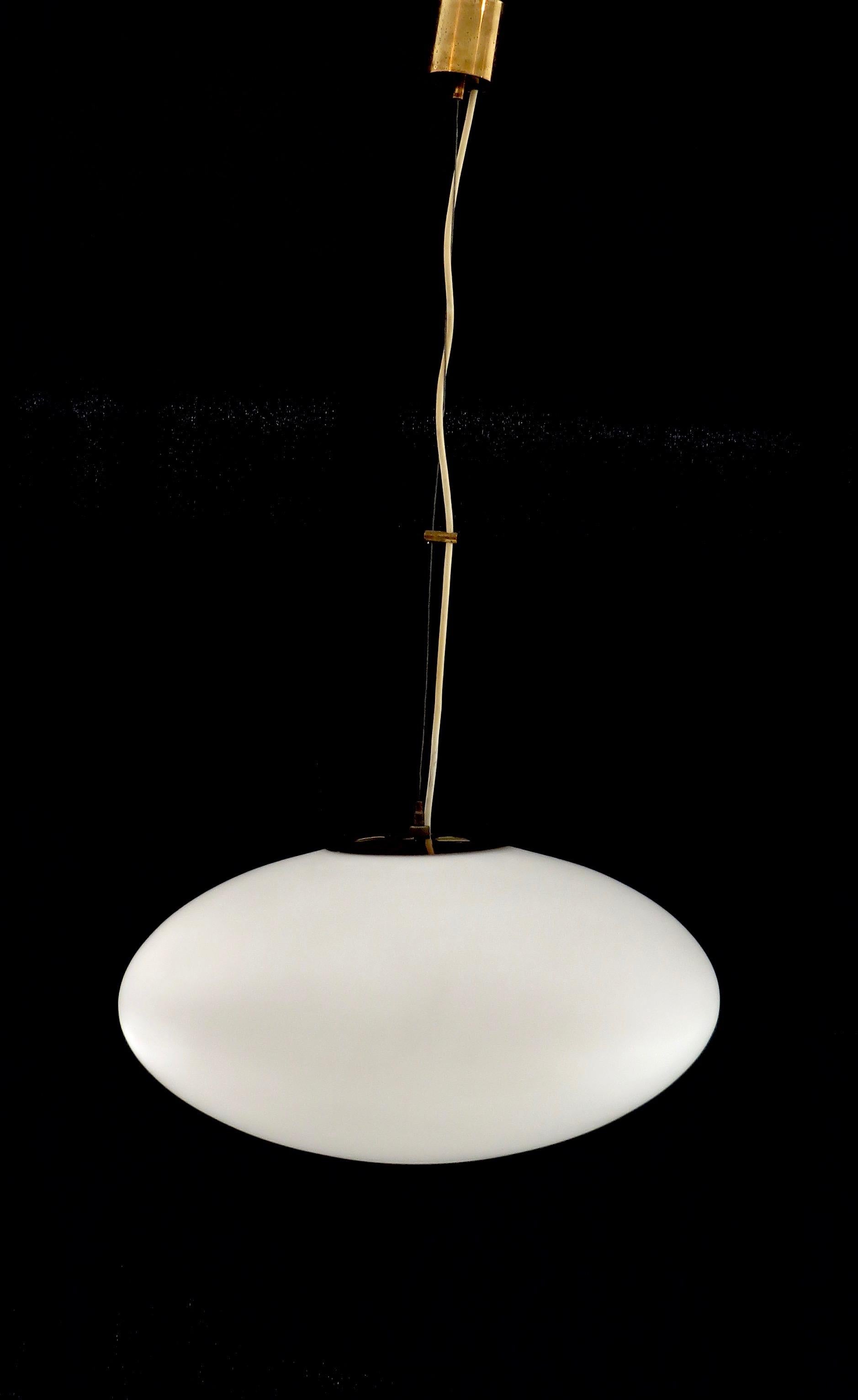 An elliptical shaped pendant chandelier of blown matte white opaque glass with brass fittings. Single light source, max 100W. Original Italian brass ceiling canopy by Stilnovo, circa 1960. The canopy can be adapted to USA canopy.
Length drop can be