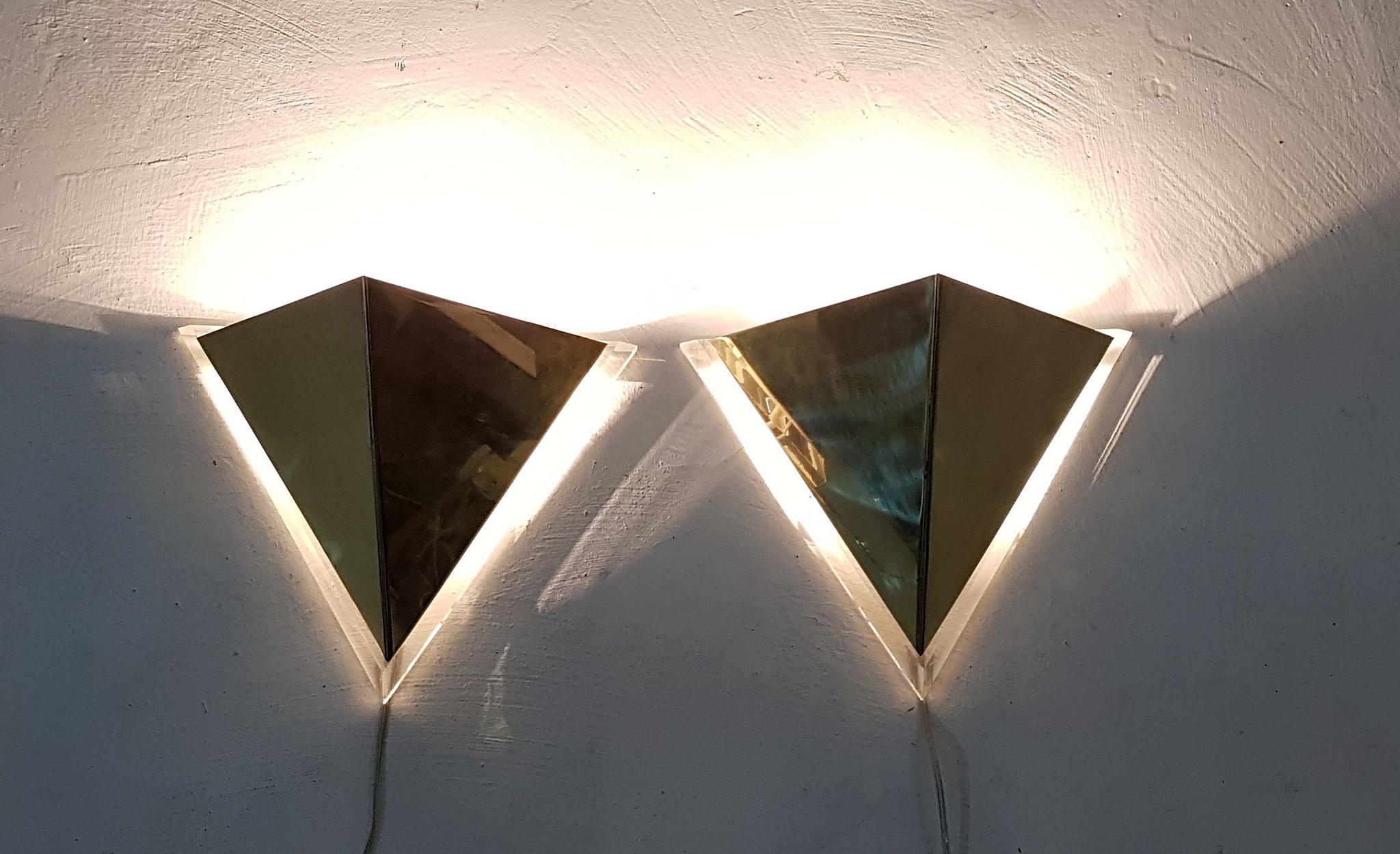 Pair of vintage wall sconces with a clean triangular design in Lucite and brass. The lampshade is mounted on hinges which makes it easy to change lightbulbs. Excellent condition. Uses an E40 lightbulb.