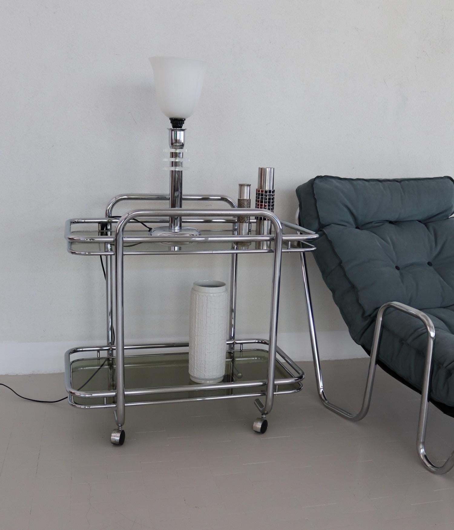Elegant service trolley or bar cart with chromed metal frame and 4 rollers.
The glasses are smoked in light brown-grey and are in very good vintage condition.
The trolley can be used as a bar cart, but is very nice also to use as a side