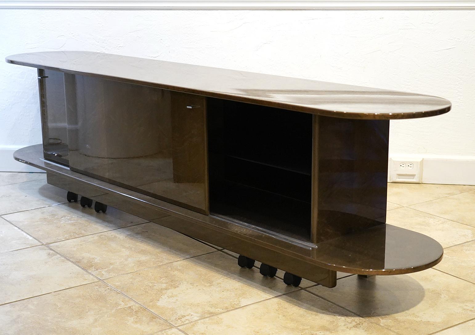 This Italian design credenza features a long top with rounded ends corresponding with a bottom of identical size and design. Between those two levels sliding doors open up to glass shelved interiors creating an elegant minimalist horizontal effect.