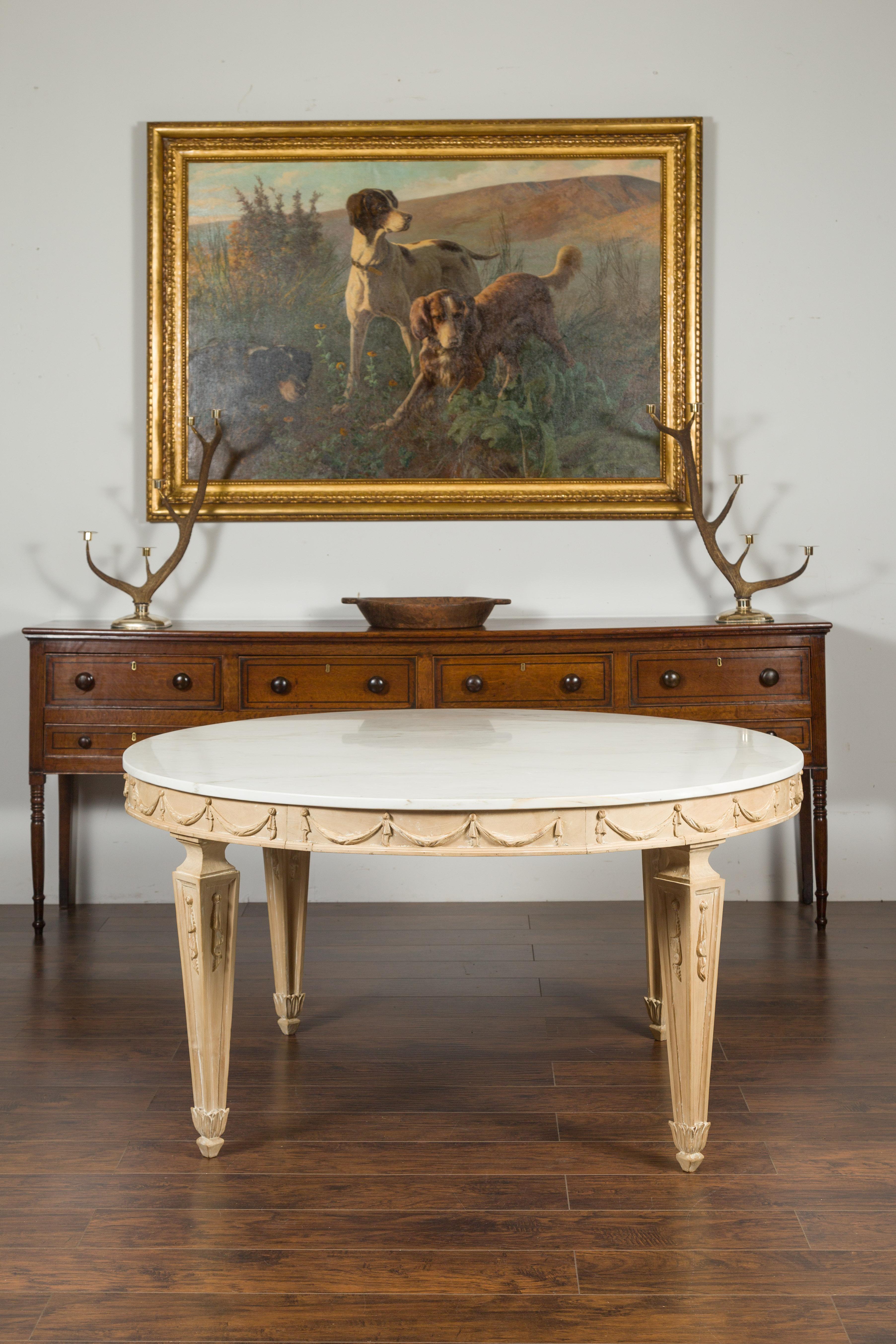 An Italian vintage neoclassical style pine dining room table from the mid-20th century, with white marble top, carved swags and tapered legs. Created in Italy during the mid-20th century, this exquisite dining table features a circular white veined