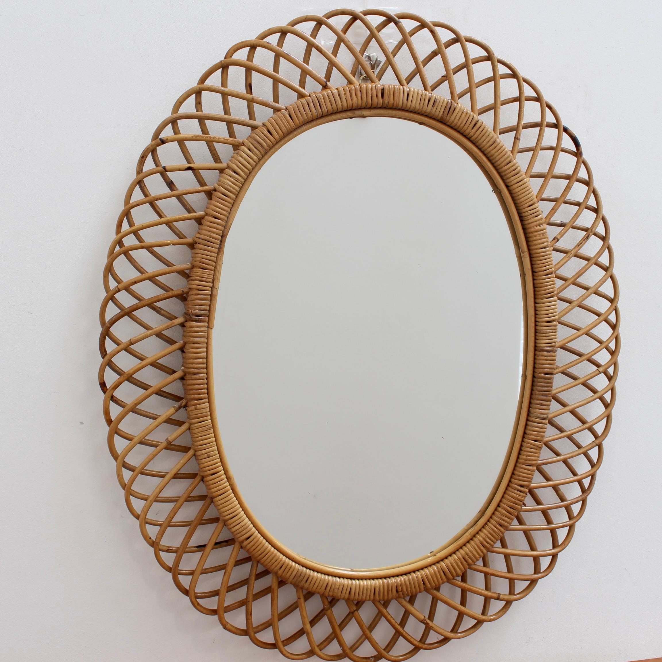 Italian rattan wall mirror (circa 1960s). This mirror has a complex weave of rattan in a continual series of horseshoe-shaped projections on the frame edge. The mirror is in overall good condition. There is a graceful, aged patina on the mirror