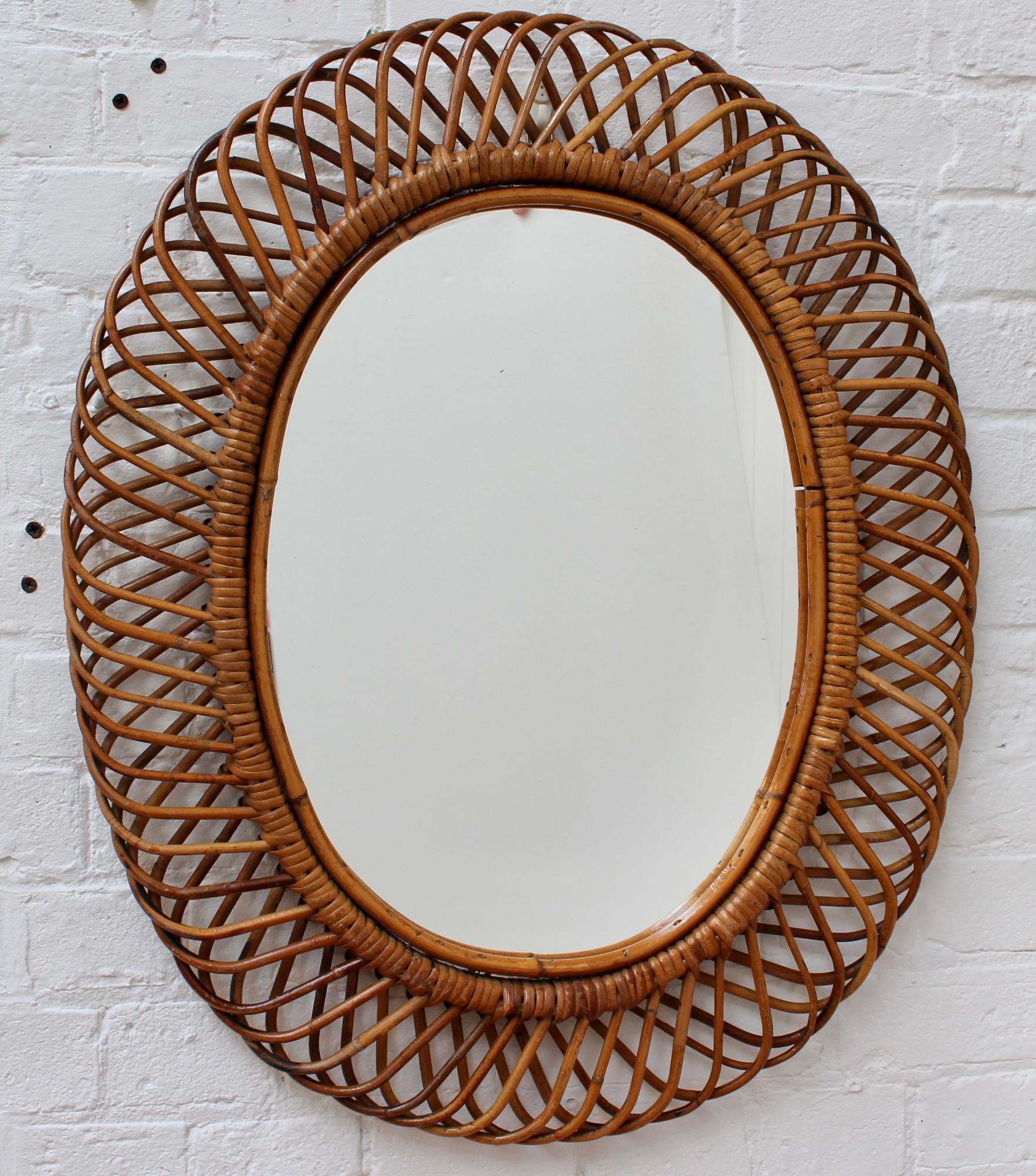 Vintage Italian oval rattan wall mirror (circa 1960s). This mirror has a complex weave of rattan in a series of horseshoe-shaped projections on the frame edge. There is a graceful, aged patina on the mirror frame and the rattan wrap-around ties have