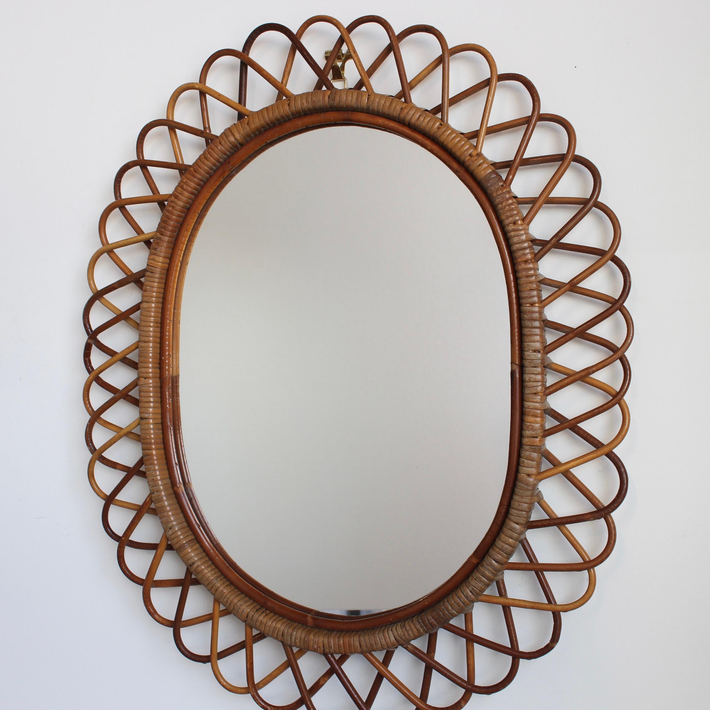 Wandspiegel aus Rattan (ca. 1960er Jahre) in dem unnachahmlichen italienischen Stil, der so beliebt ist. Dieser Spiegel hat ein reizvolles Rattangeflecht, das sich in einer Reihe von hufeisenförmigen Vorsprüngen am Rand des Rahmens fortsetzt. Es