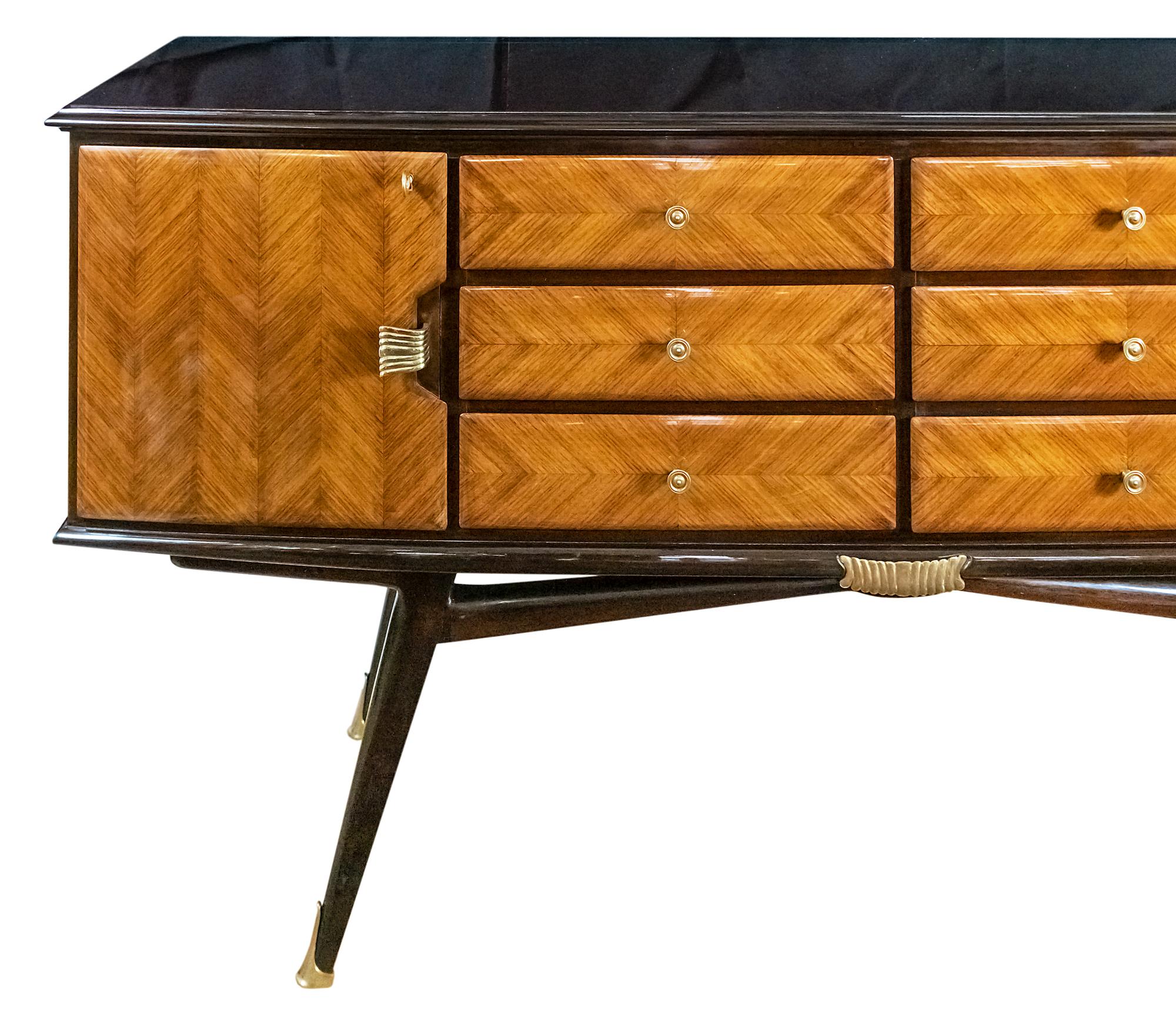 Italian vintage wood veneer sideboard from 1950s.
Wood surface is varnished, the drawers are decorated with brass handles, side doors are with keys.
Legs are with decorative brass details.
The top is glass.
Very good vintage condition, after