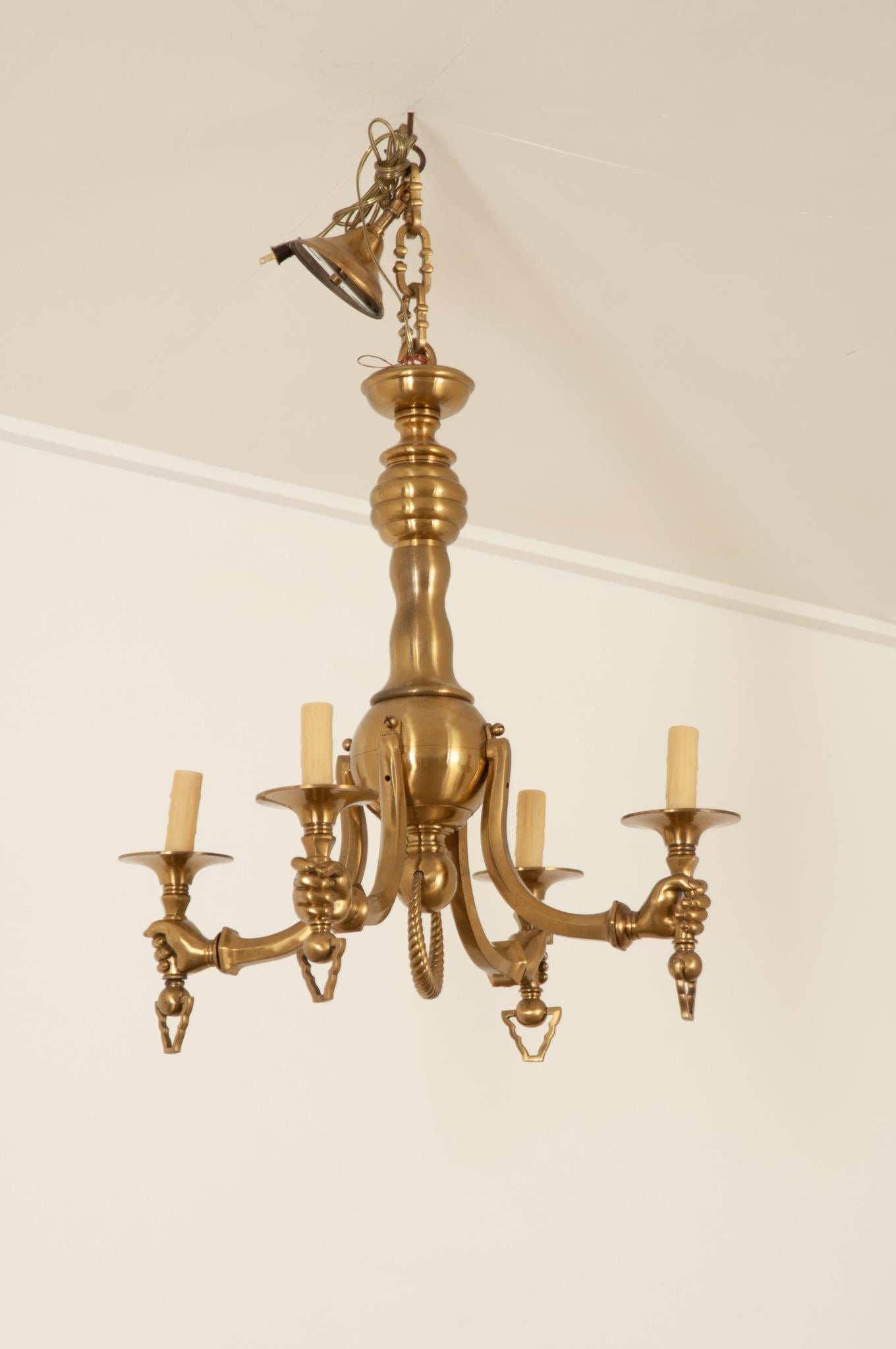 A striking solid brass chandelier from Italy in fantastic vintage condition. The four arms terminate with realistic human hands holding the candlestick. Cream, faux melting candle covers hide the sockets. A decorative chain supports the fixture and