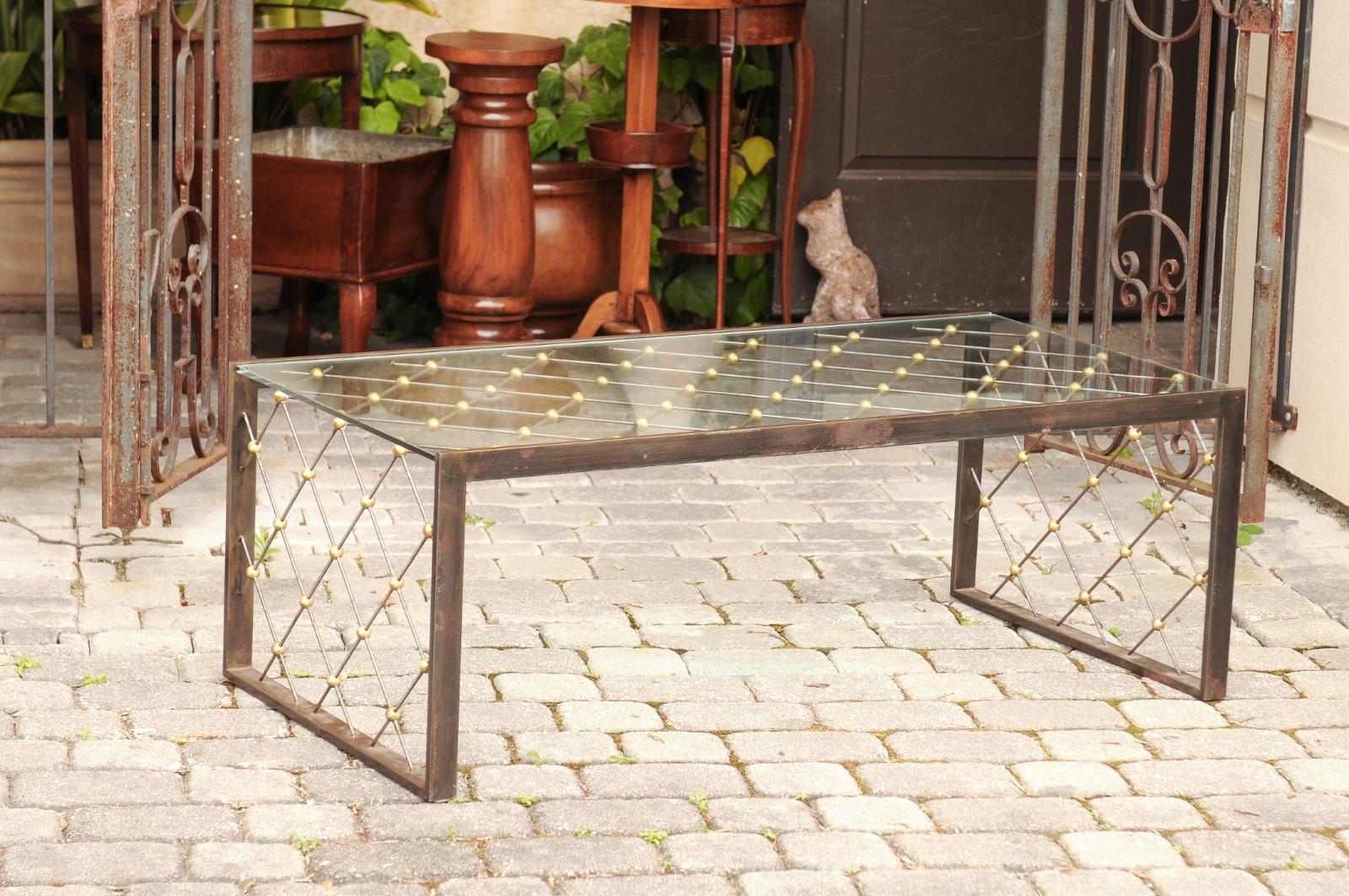 A French steel and brass cocktail table from the mid-20th century, with glass top and diamond patterns in the style of and attributed to Jean Royere. Born in France during the mid-century period, this stylish cocktail table features a rectangular