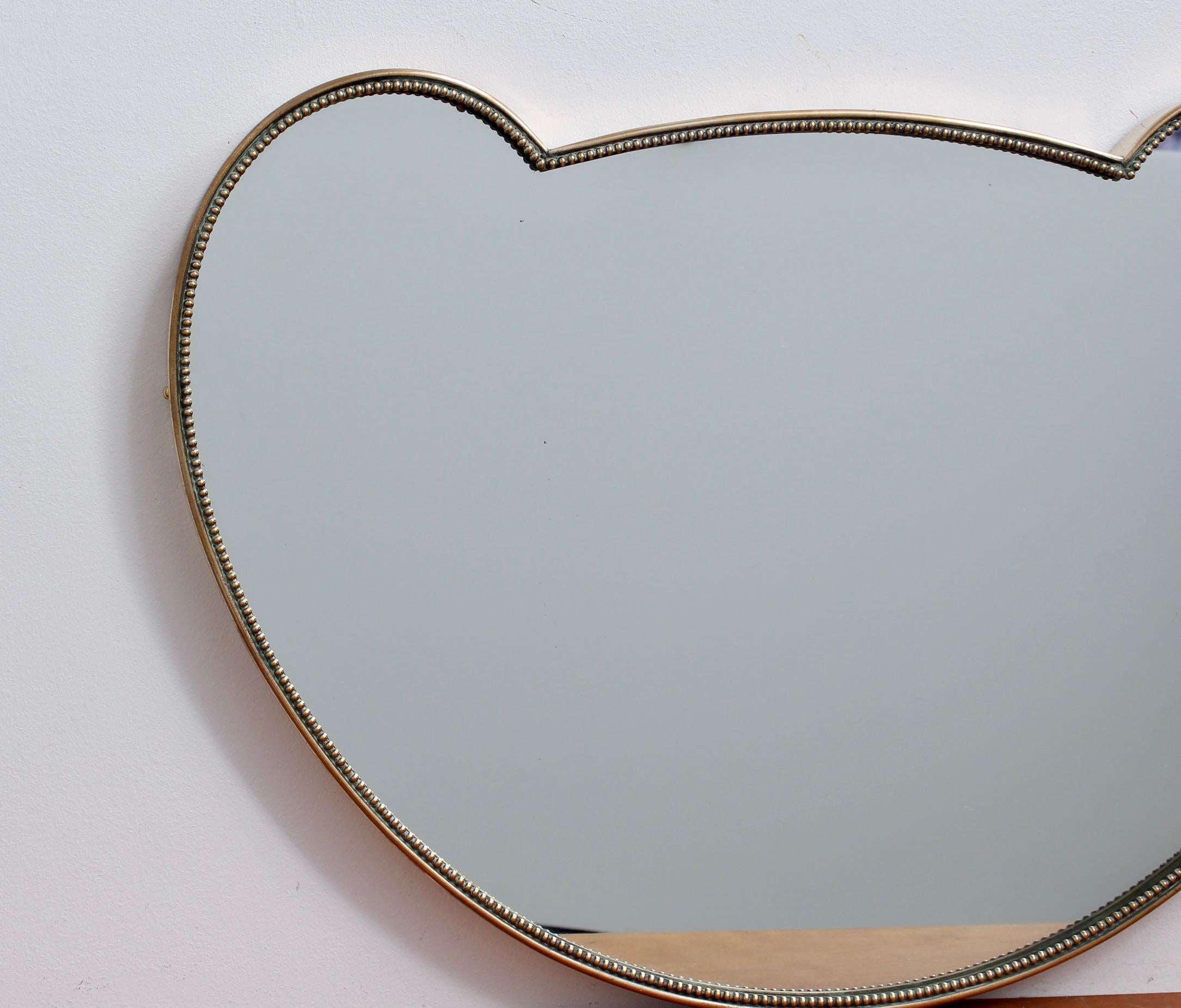 Small Mid-Century Italian wall mirror with brass frame (circa 1950s). The mirror is of a rare shape (Mickey Mouse ears?) combining sumptuous curves and a lovely beading surrounding the frame to add further interest. It is classically elegant and