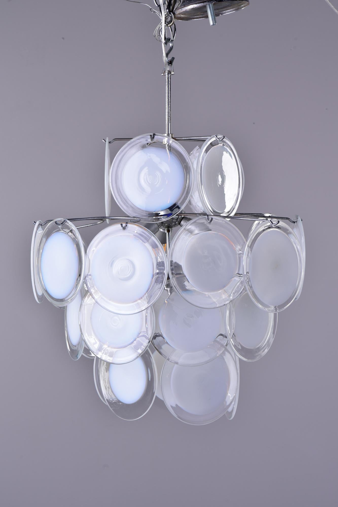Circa 1960s Vistosi style murano glass fixture with four tiered metal frame hung with round art glass disks that are clear at edges and more opaque white at the center. No maker's mark. Six candelabra sized sockets. New wiring for US electrical