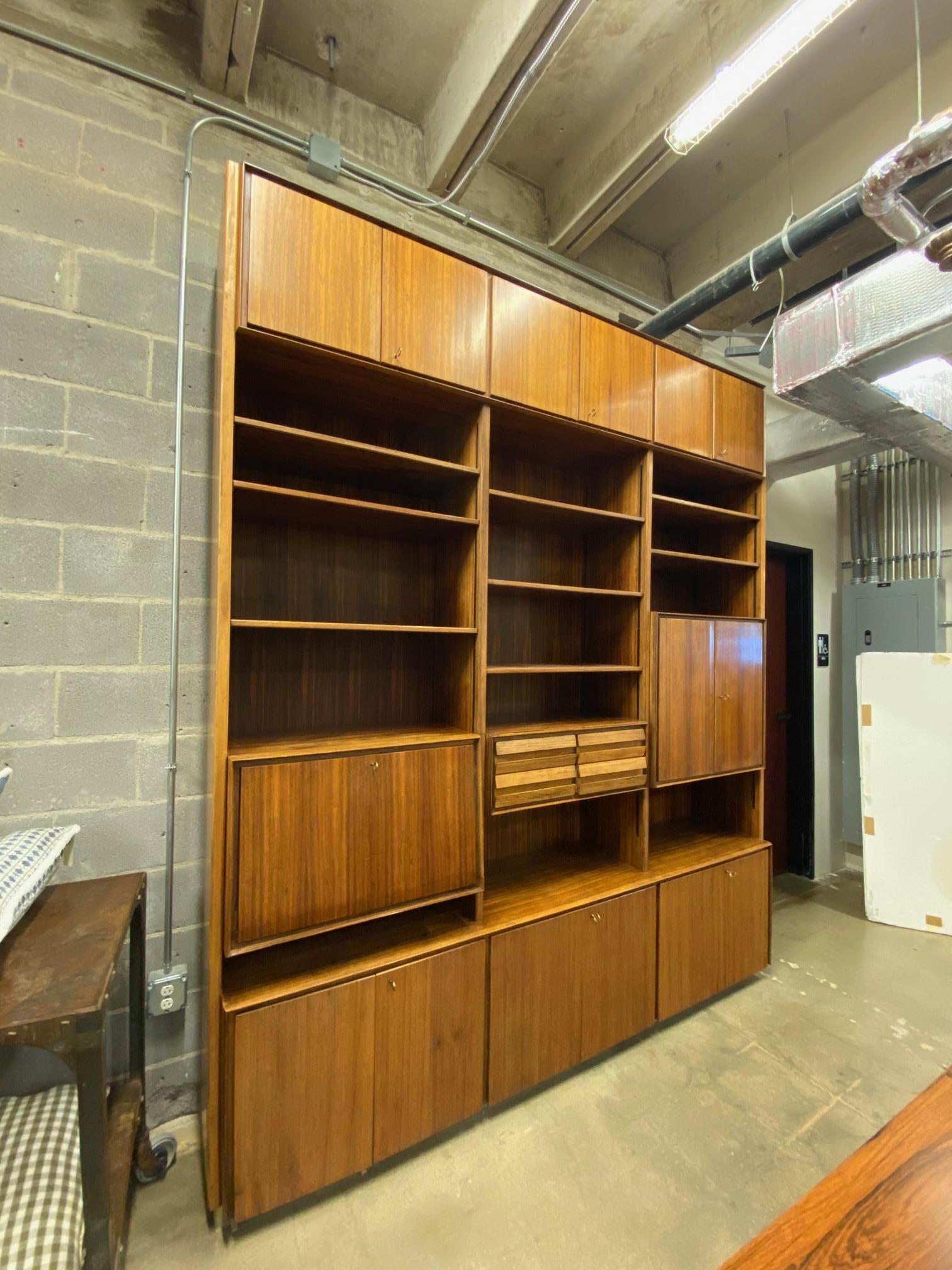 Italian mid-century modern large rosewood bookcase, designed by Vittorio Dassi, c. 1960, having three sets of double door cabinets above shelves.  The unit is centered with drawers, flanked by a front door, opening to drawers and compartments, and