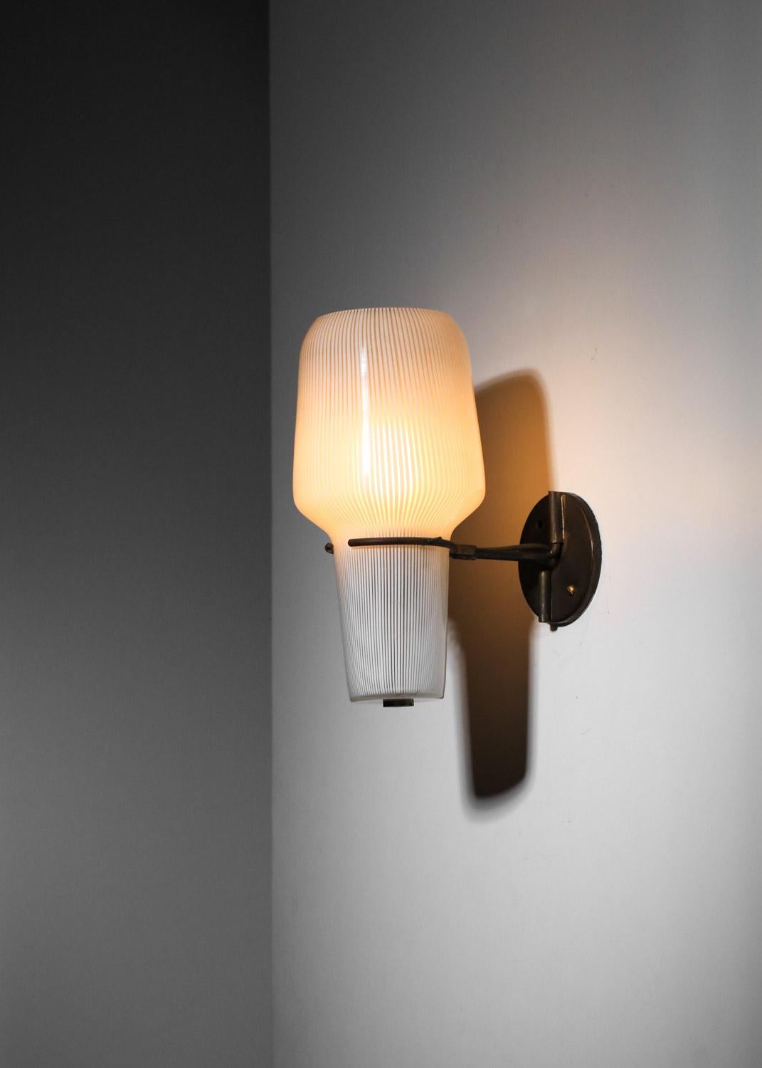 Grande lampada da parete italiana degli anni '50 attribuita a Massimo Vignelli per Venini. Struttura in ottone massiccio con patina e grande paralume in vetro di Murano bianco striato. Condizioni vintage molto buone, lievi segni di usura sulla
