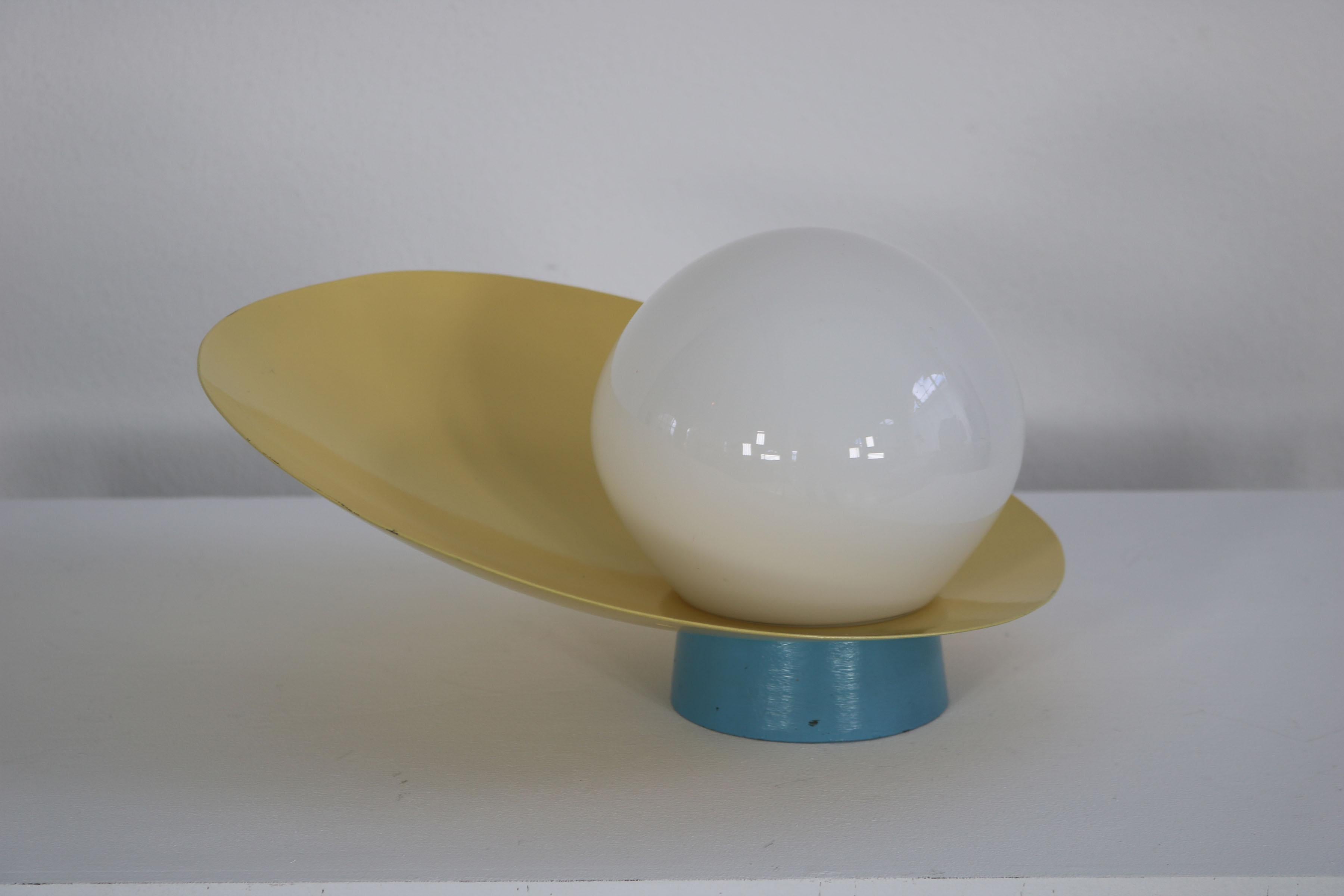 Italian decorative wall lamp from the 1960s. The light blue base of the lamp is a cast iron that shows slight signs of use especially on the bottom of the lamp. The yellow shade of the lamp is made of aluminum and the white glass ball in the center