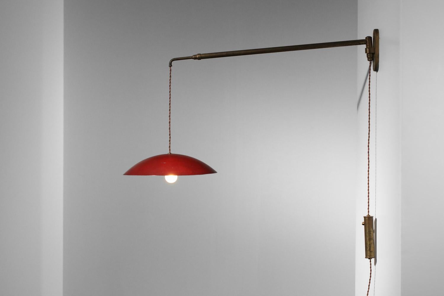 Italian wall sconce from the 50's attributed to Arredoluce. Sconce structure in solid patinated brass, lampshade in red lacquered metal (original paint). Raise and lower system allows the height of the shade to be adapted and the length of the