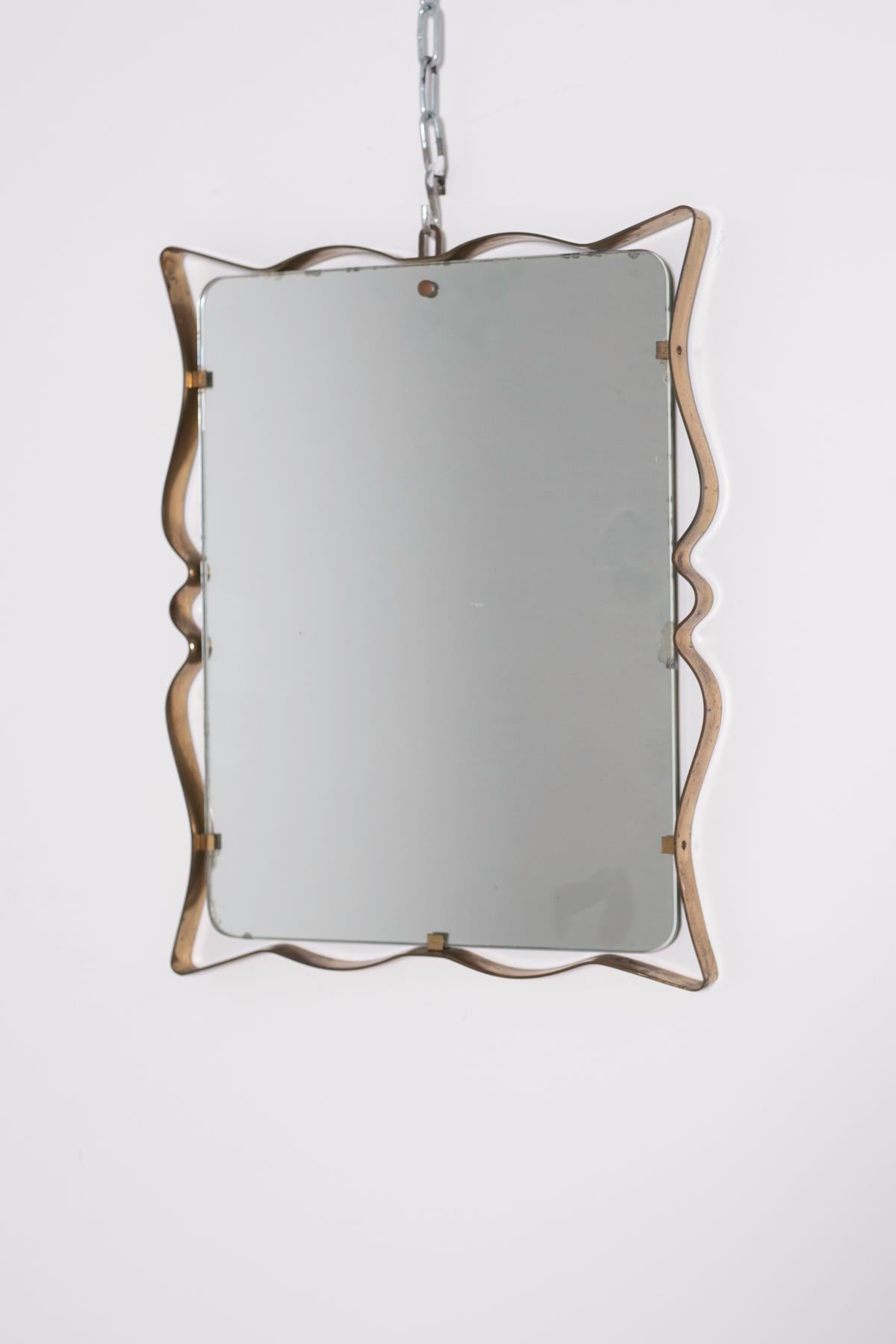 Elegant and sophisticated wall mirror produced by Fontana Arte, Italy, circa 1950.
The mirror has a shaped profile in brass curves that creates a delicate undulation to the object. Its brass profile is detached from the glass and connected to the