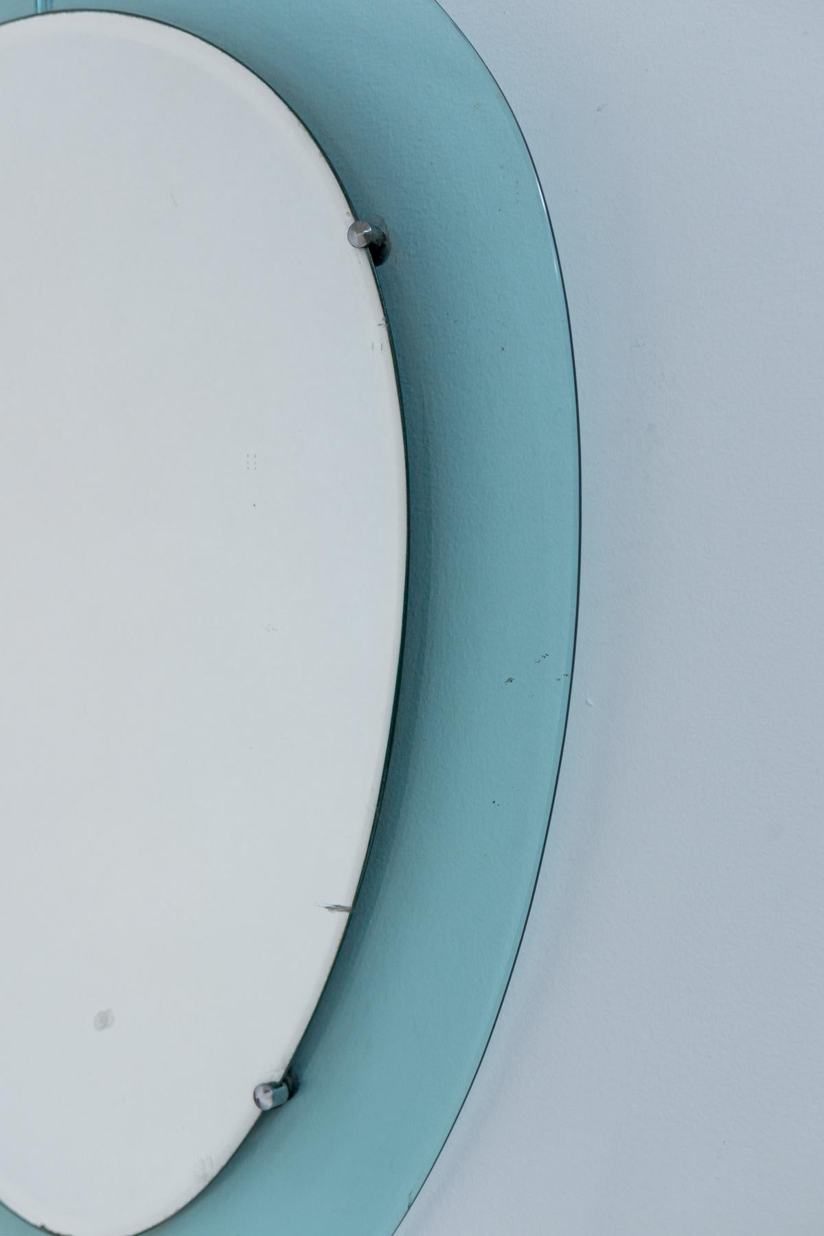 Eccentric and elegant wall mirror of Italian manufacture from the 1950s. 
The mirror is oval in shape and its special feature is its blue glass border around the perimeter. In the central part we find its mirror glass in excellent condition hooked