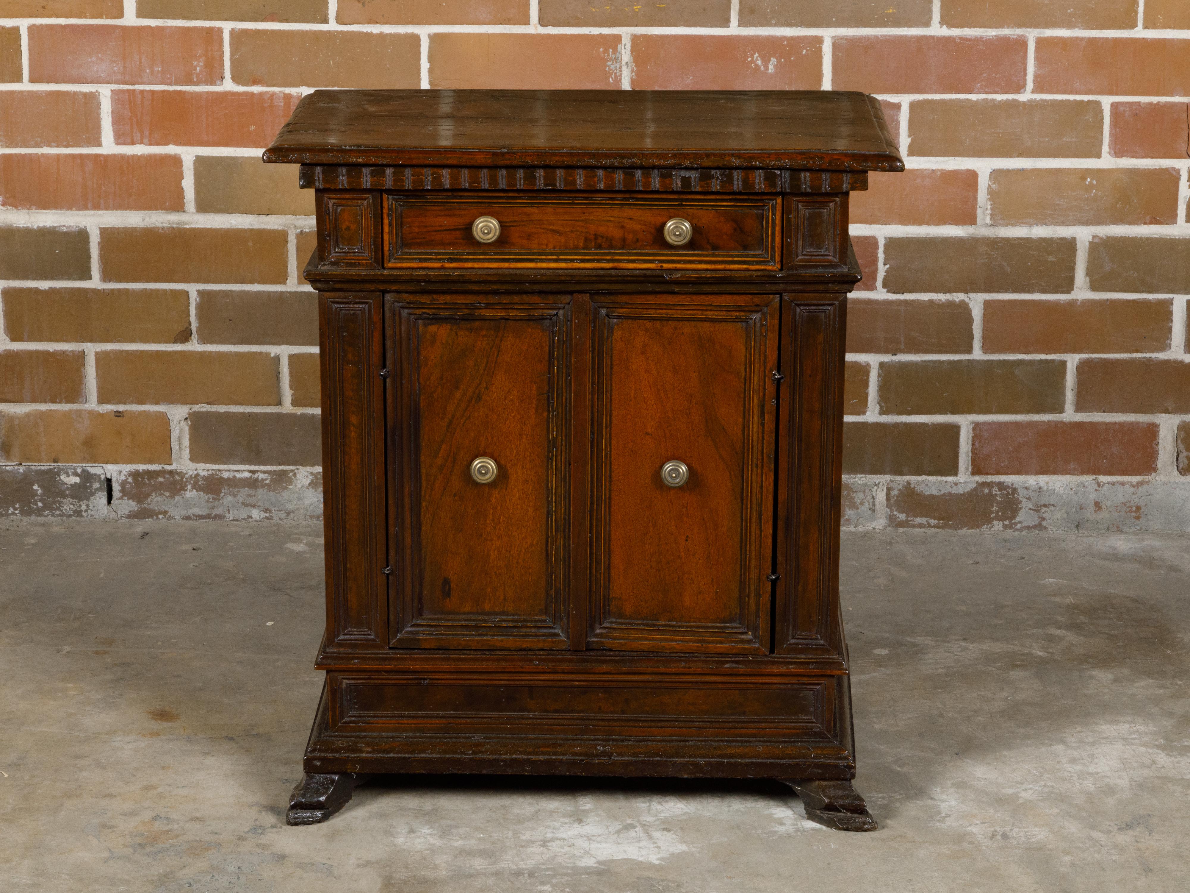 An Italian walnut credenzino from the 19th century with single drawer, petite double doors, carved dentil molding and feet. This Italian walnut credenzino from the 19th century is a masterpiece of craftsmanship and elegance, combining utility with