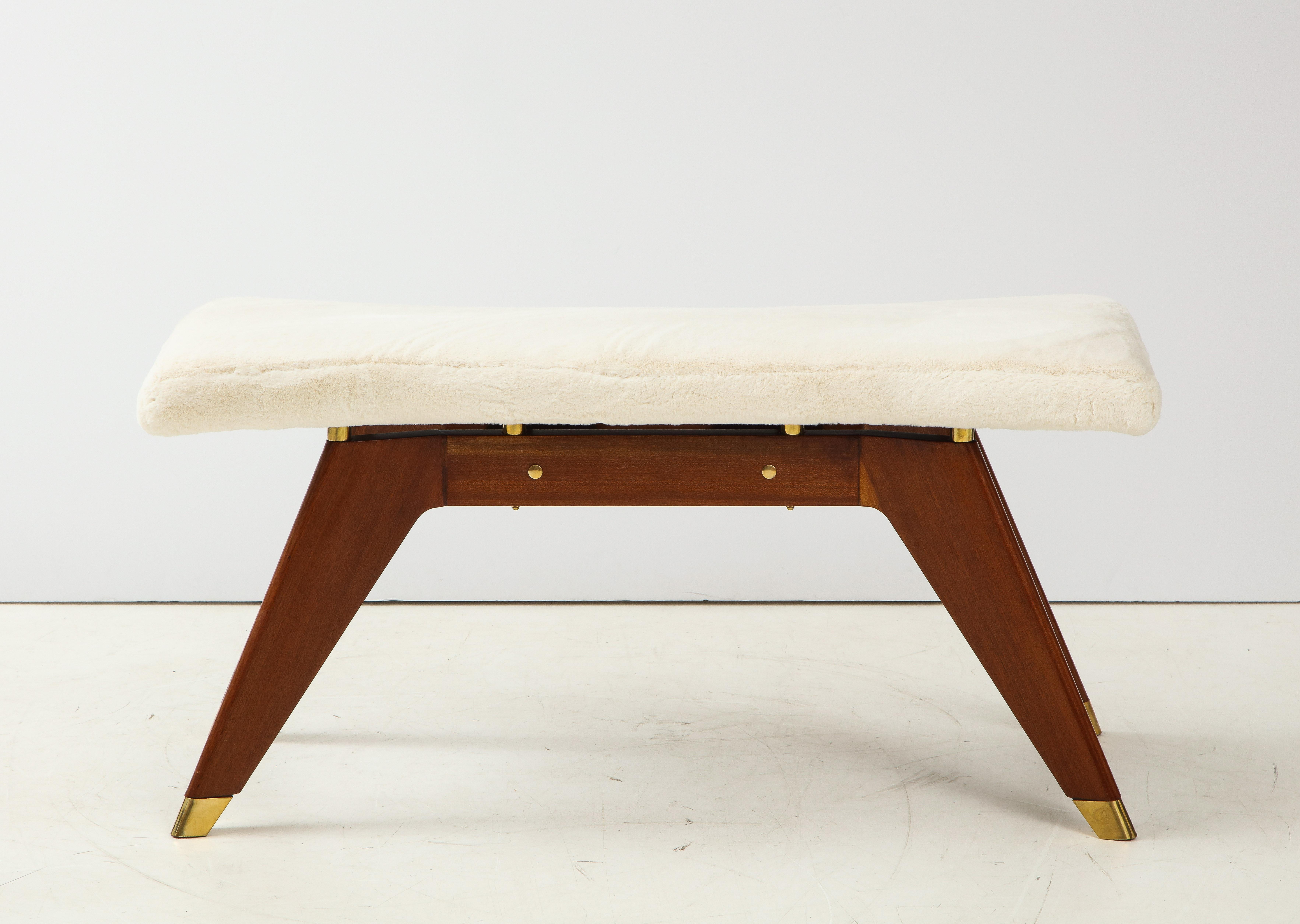 A stunning Northern Italian 1940s walnut bench, featuring angled and tapered legs, the feet capped in brass. The long beautifully shaped seat newly reupholstered in a faux creamy colored fur and separated by eight brass cylindrical shaped supports.