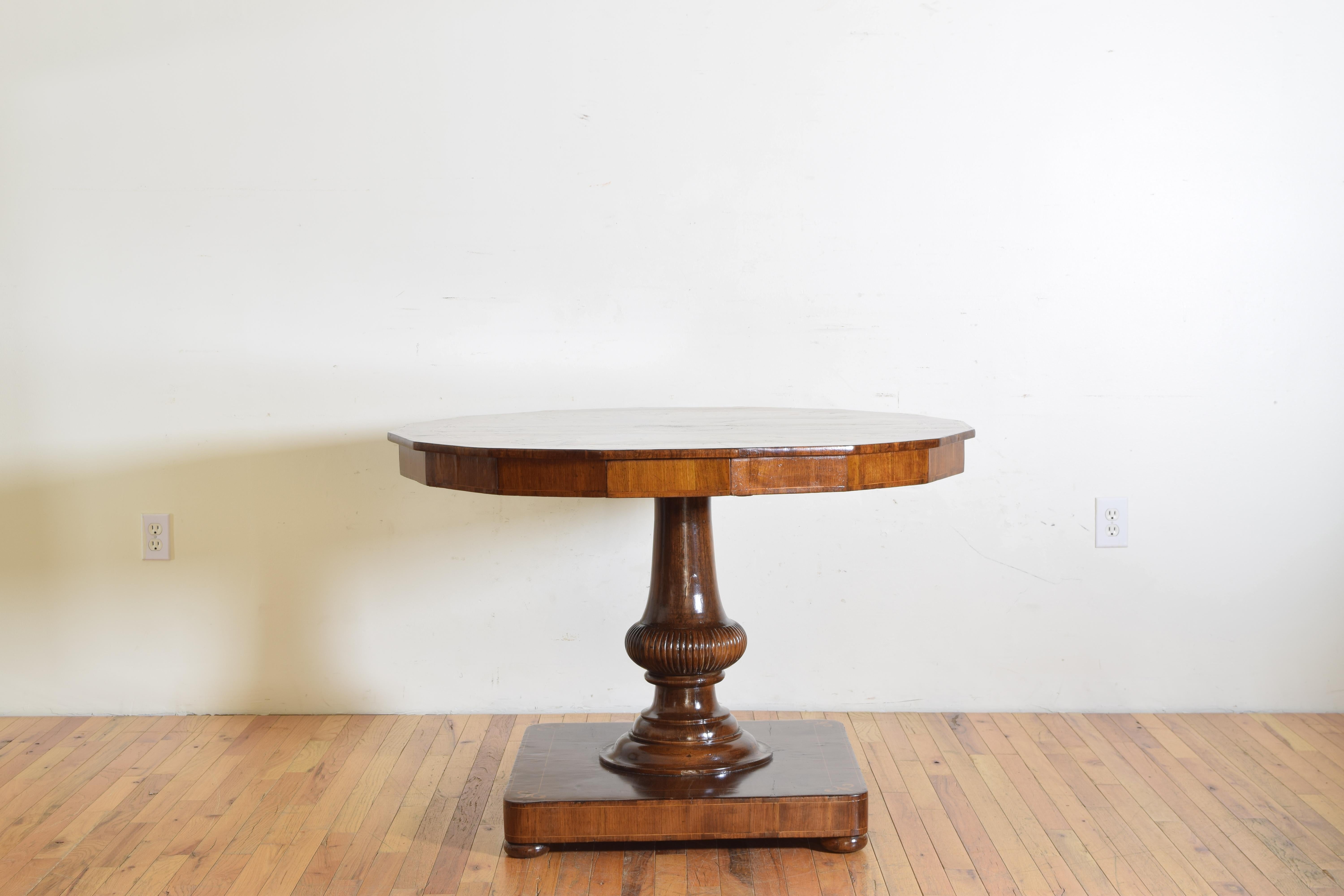 A hexadecanoic shaped tabletop is Inlaid with fruitwood fleur-de-lis, a stylized lily, symbolizing life, perfection, and light. The central pedestal is shaped, carved, and raised on a veneered and inlaid plinth base with matching fleur-de-lis in the