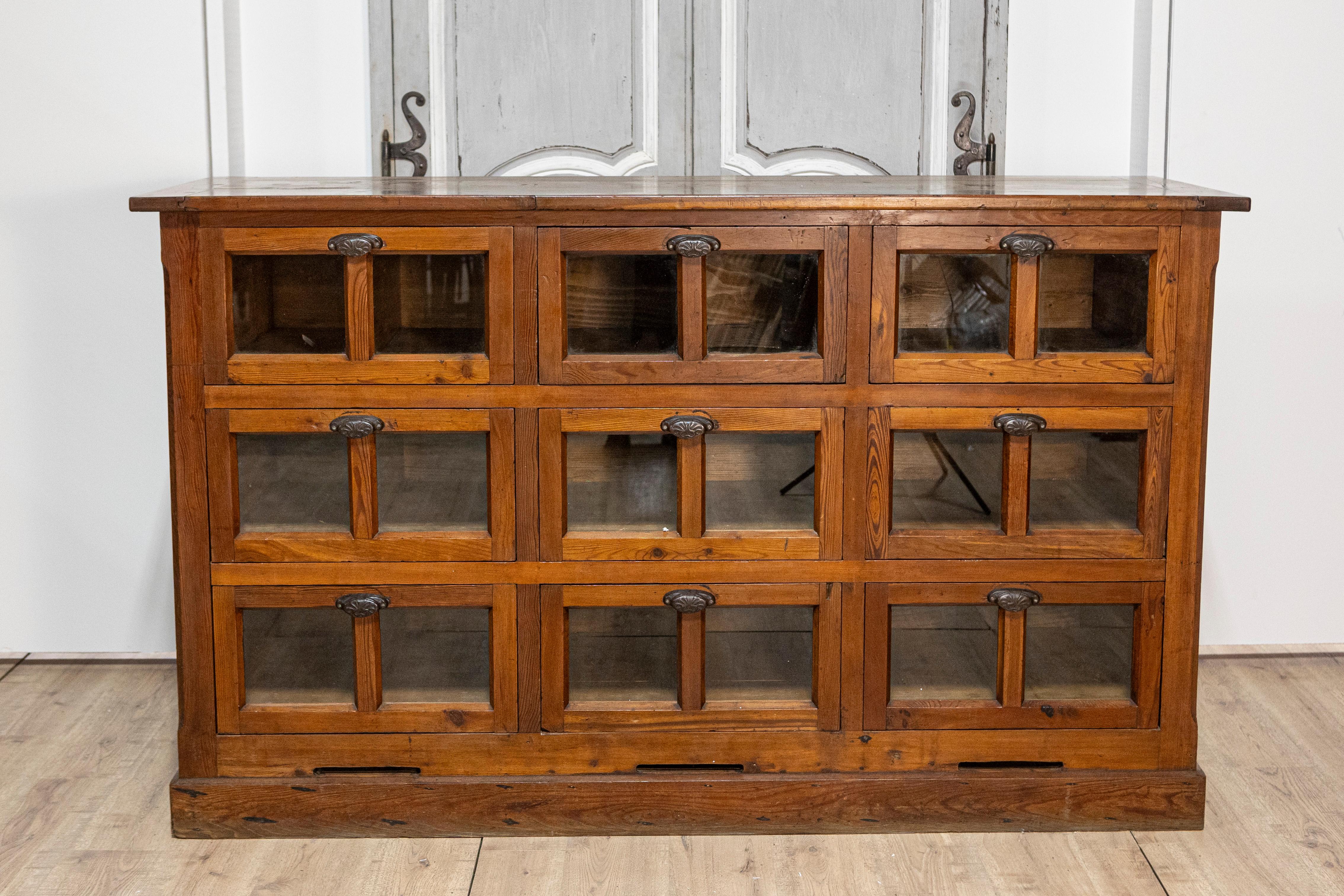 An Italian walnut pastaia shop cabinet from the 20th century with nine drawers, glass panels and iron hardware. Crafted in Italy during the 20th century, this elegant walnut pastaia shop cabinet captivates with its apothecary-inspired design and