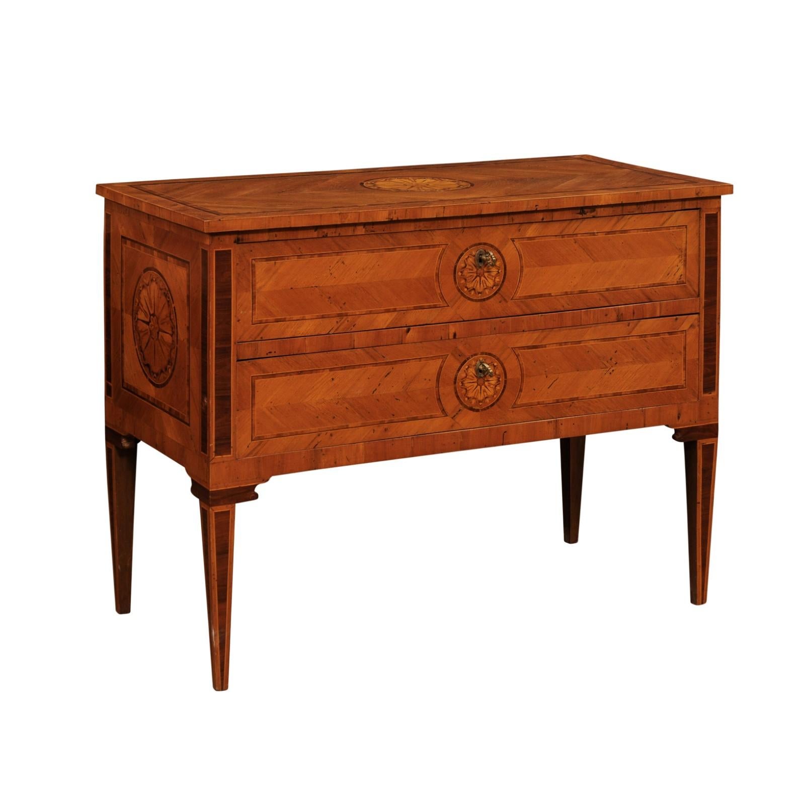 An Italian walnut and mahogany commode from circa 1900 with two drawers, marquetry, cross-banding and tapered legs. Delve into the world of Italian elegance with this circa 1900 Italian commode, a masterpiece of craftsmanship and design. This