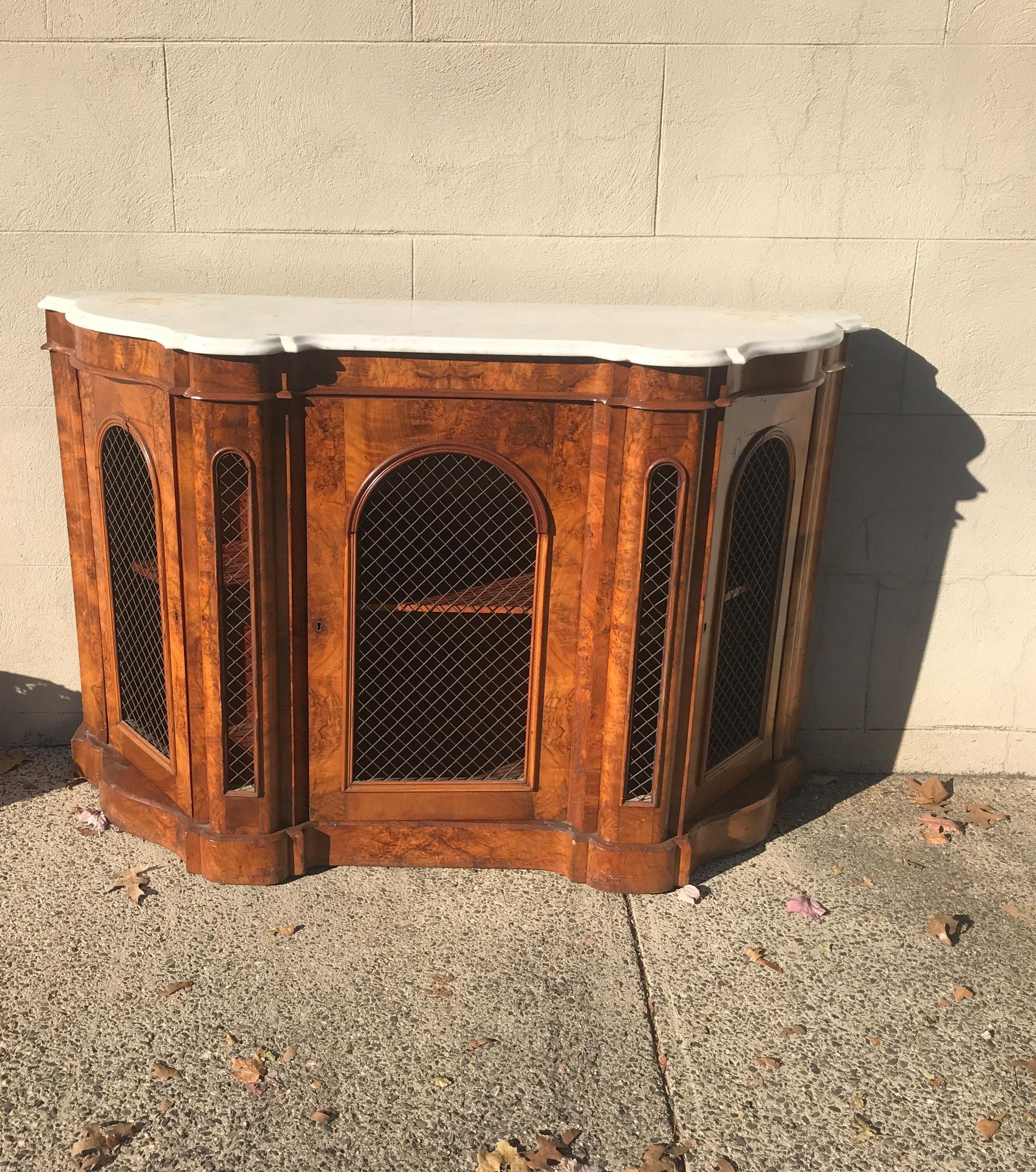 Beautiful Italian walnut credenza with original marble top. A center door flanked by a door on each side. The opening on the doors are covered by brass lattice grates. The interior with a single shelf. In very good original well cared for condition
