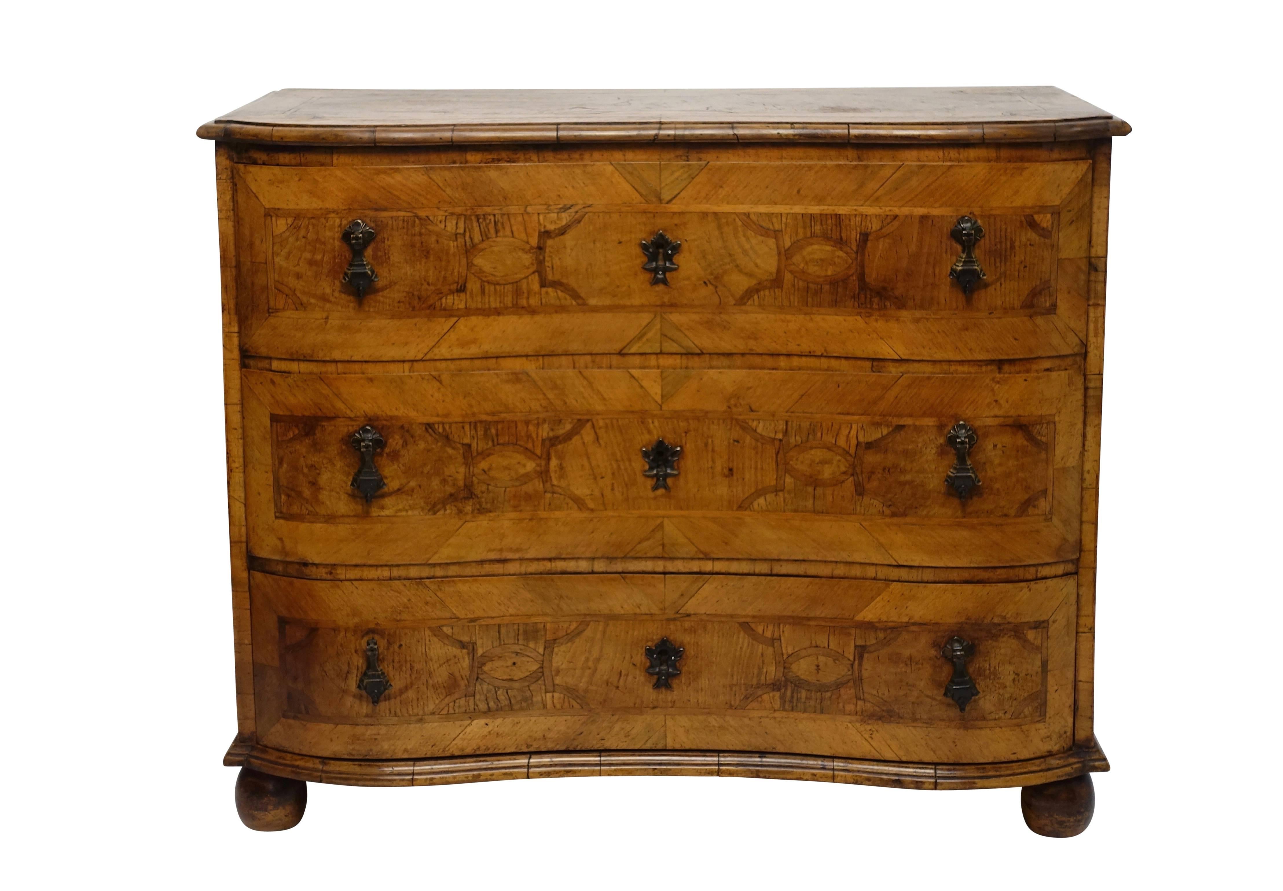 A fine and beautifully made serpentine shape walnut three-drawer commode or chest of drawers with olivewood inlay. Geometric pattern inlay on the sides, top and drawer fronts, and having patinated brass pulls, sitting on bun feet, Italian, early to