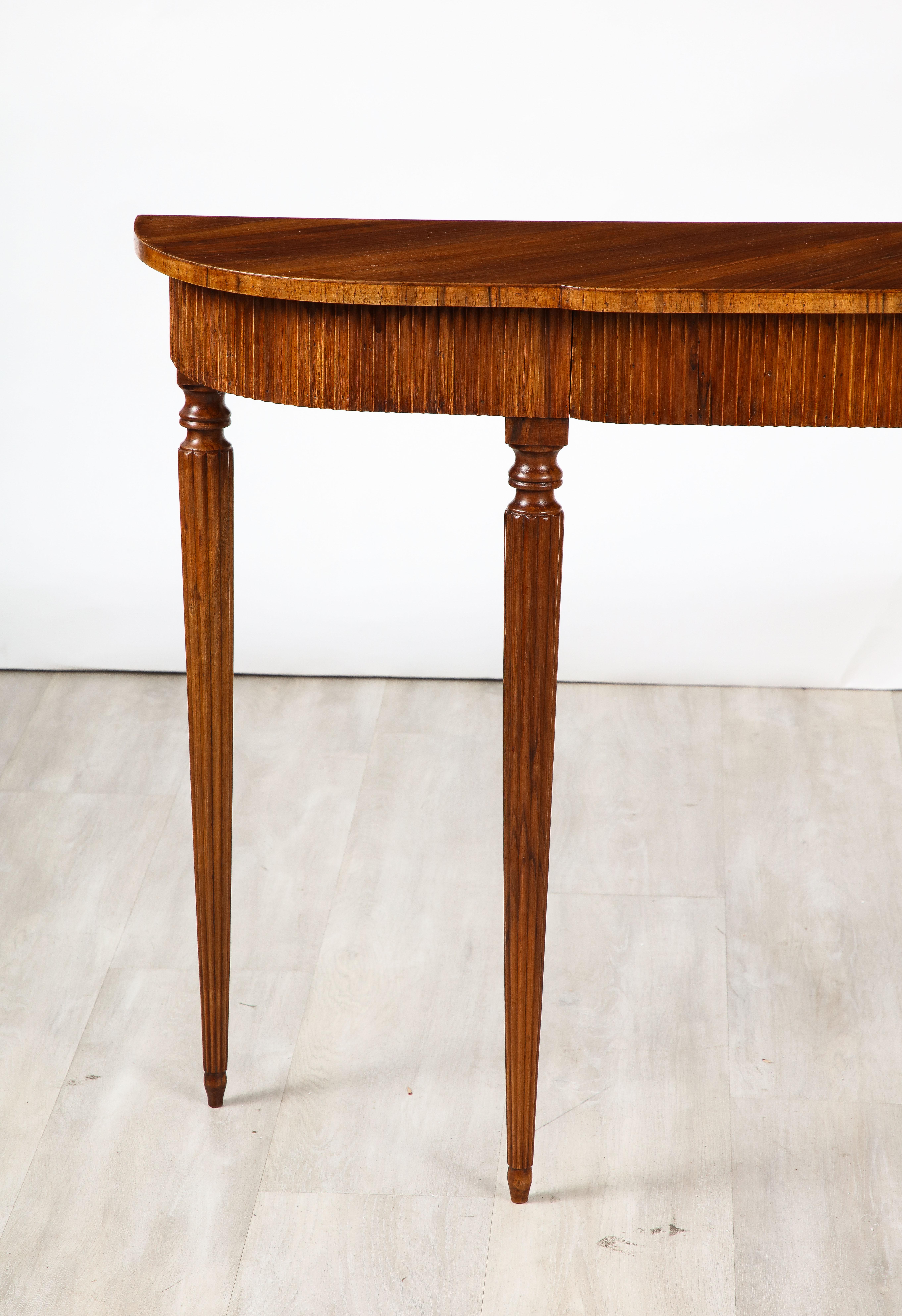 An elegantly appointed Italian 1930's walnut console table, the shaped top rests upon the carved fluted motif apron consisting of two hidden drawers,  the whole supported on four tapered and fluted legs ending in chic toupie feet. 
Northern Italy,