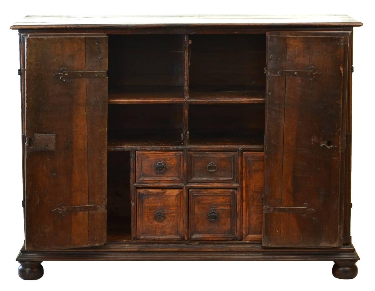 17th century Italian walnut credenza, the rectangular top over the bi-fold doors, each with lozenge molding and wrought iron strap-work; the interior fitted with shelves and drawers, on replaced bun feet.

This credenza has beautiful color and