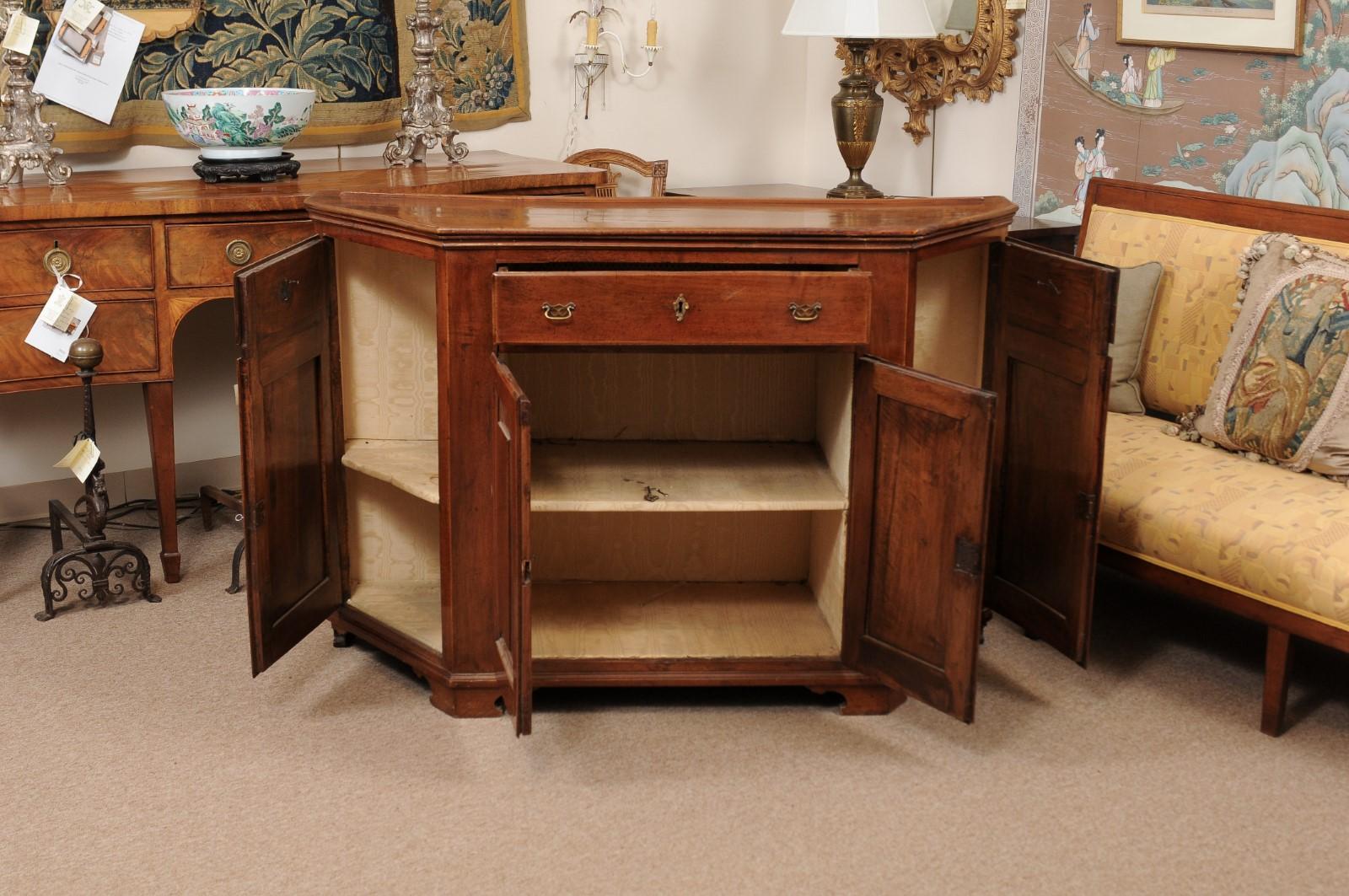 Early 19th century Italian walnut credenza with canted sides, 3 drawers with brass hardware and 4 cabinets below with raised paneling ending in carved bracket feet.