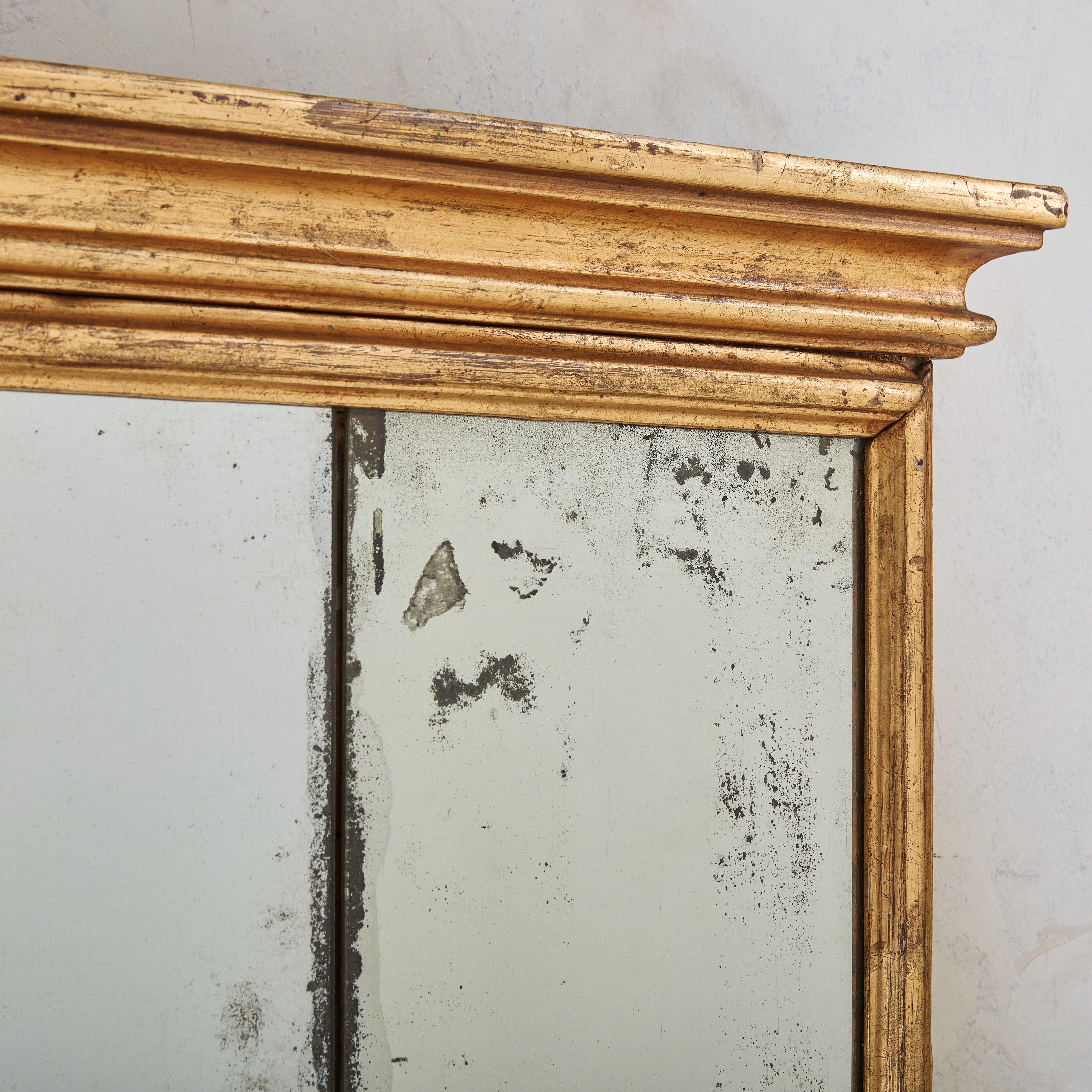 Crafted in Italy over two centuries ago, this wall mirror reflects the Baroque style. Its detailed walnut frame, finished in gilt, is defined by intricate carvings and textured accents, particularly along the top and base. The original antique
