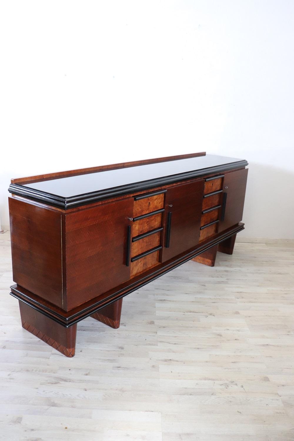 Beautiful and rare long sideboard of the period Art Deco, 1930s. Characterized by an essential and elegant line made of veneered walnut with fine walnut burl decoration on the front and ebonized profiles. The top is in thick black glass. Large
