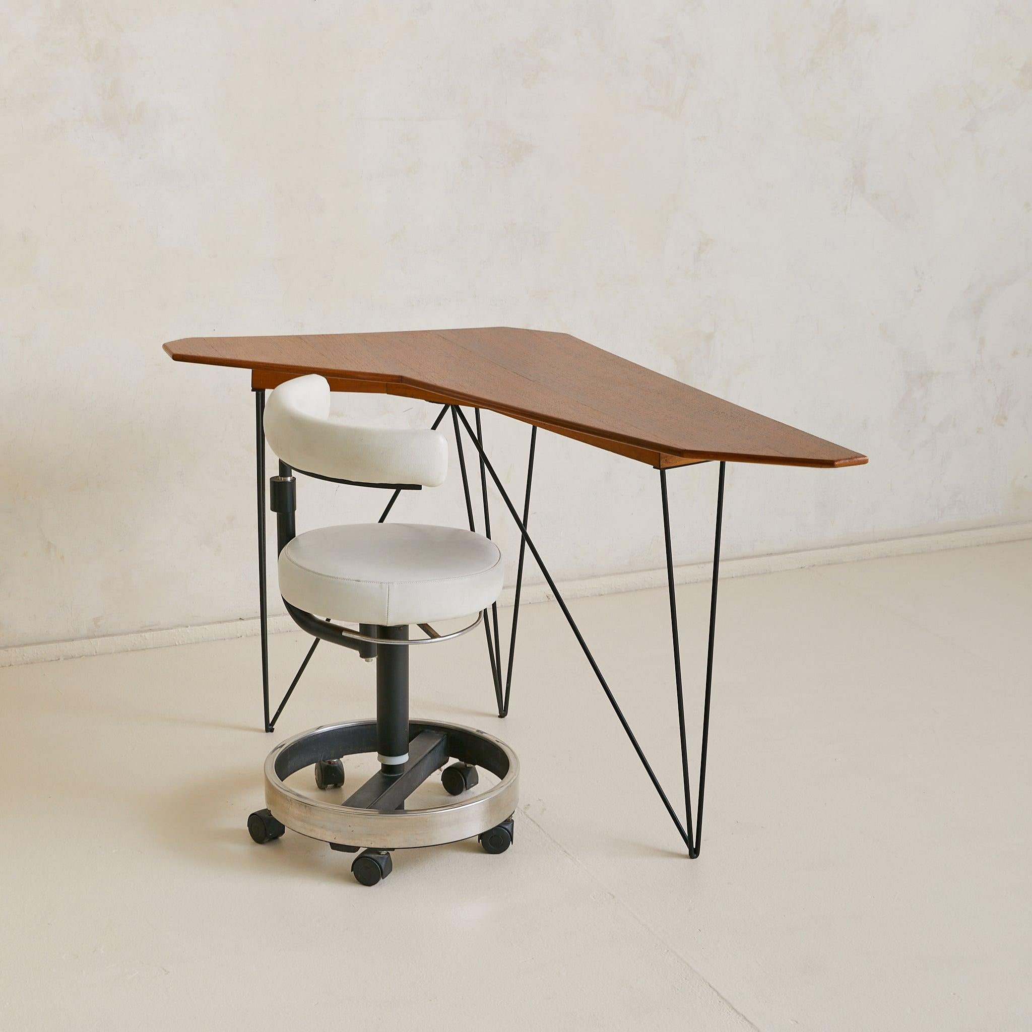 An Italian console or corner desk from the 1950s, defined by its asymmetrical profile. The walnut top is cut into a sharp, angular form, cantilevering lightly over a geometric base of blackened metal rods. The play of negative space lends the piece