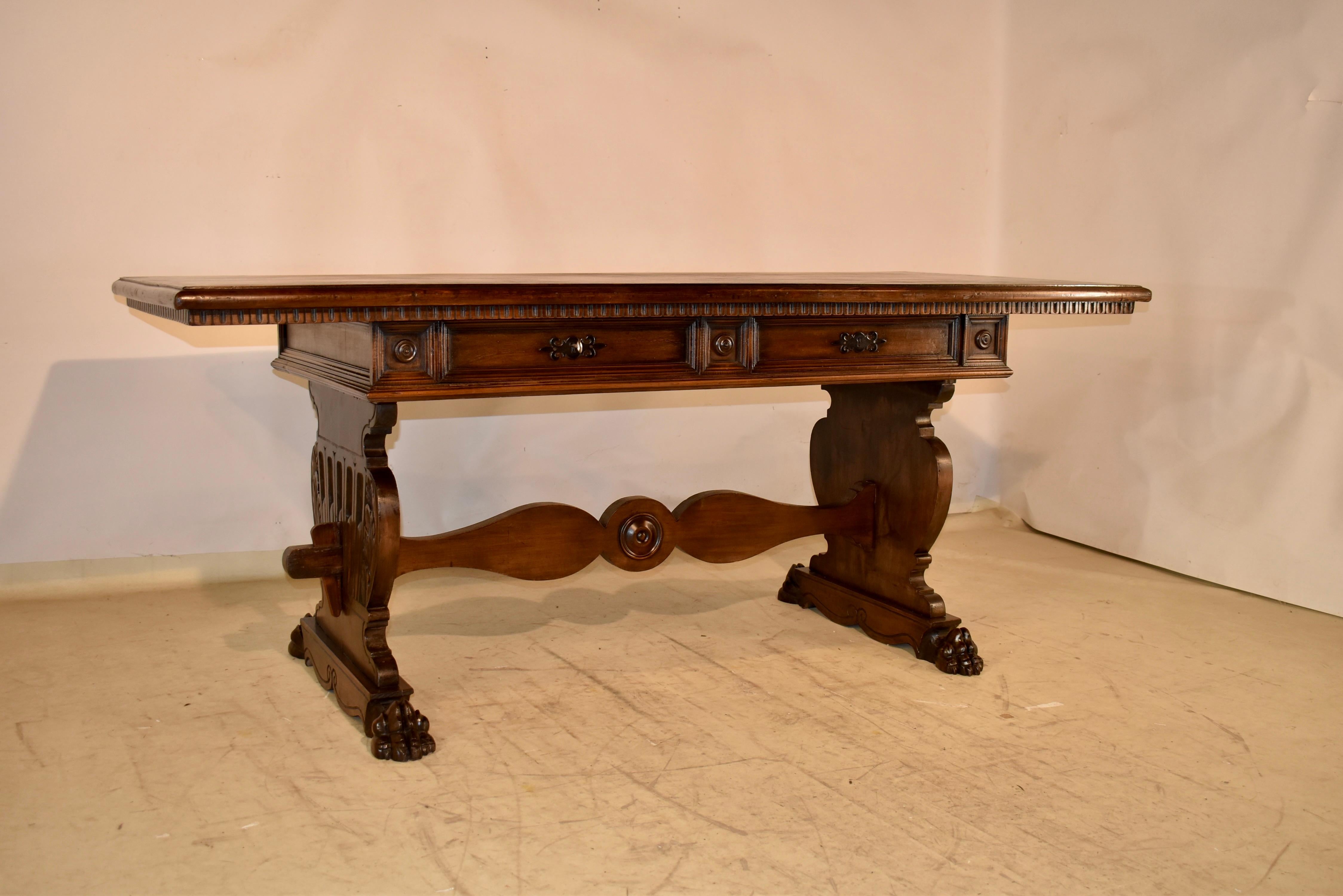 Circa 1920's walnut library table or writing desk from Italy.  The top has lovely graining and has a beveled edge with a hand carved apron beneath.  The top follows down to a raised paneled apron which contains two drawers in the front and two false
