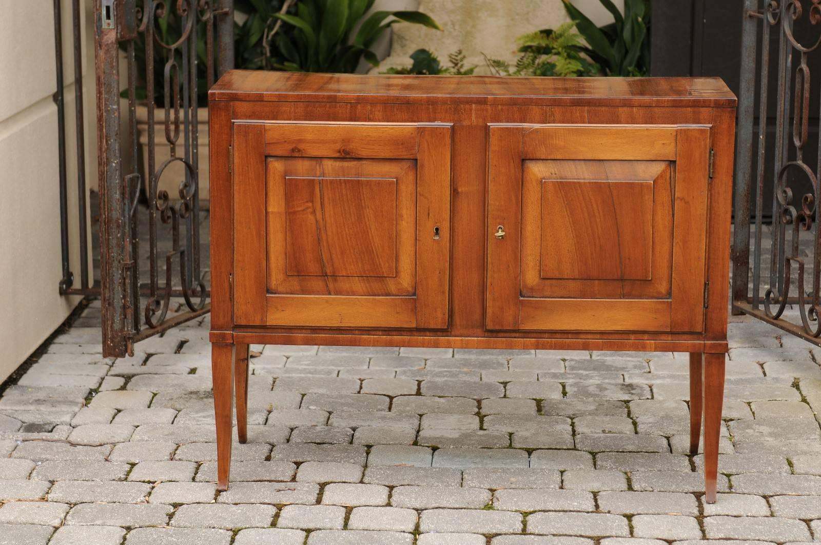 An Italian walnut or fruitwood veneered two-door credenza with slightly curved legs from the early 20th century. This Italian two-door buffet features a rectangular top sitting above two doors adorned with slightly raised panels. These doors open to