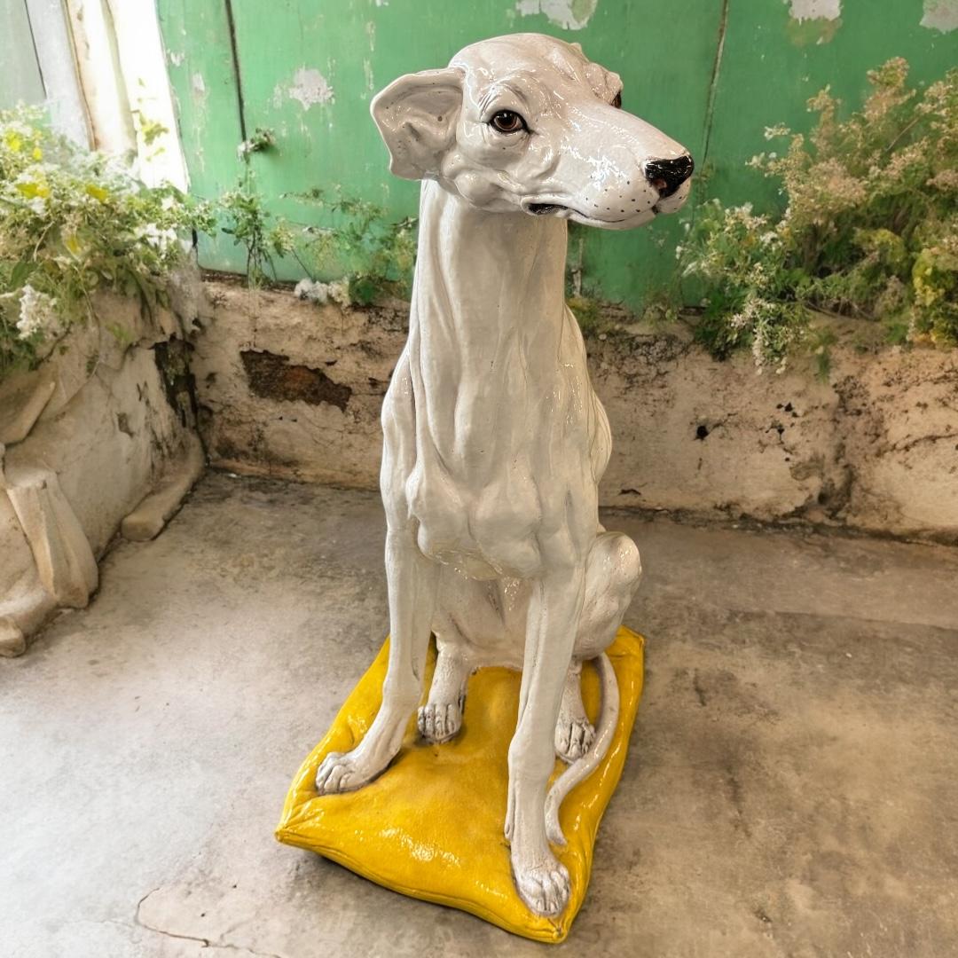 Un'eccezionale statua di levriero italiano in terracotta smaltata e dipinta a mano. Perfettamente posizionate su un piedistallo stilizzato come un cuscino, le rappresentazioni realistiche e a grandezza naturale di questo maestoso essere, severo,