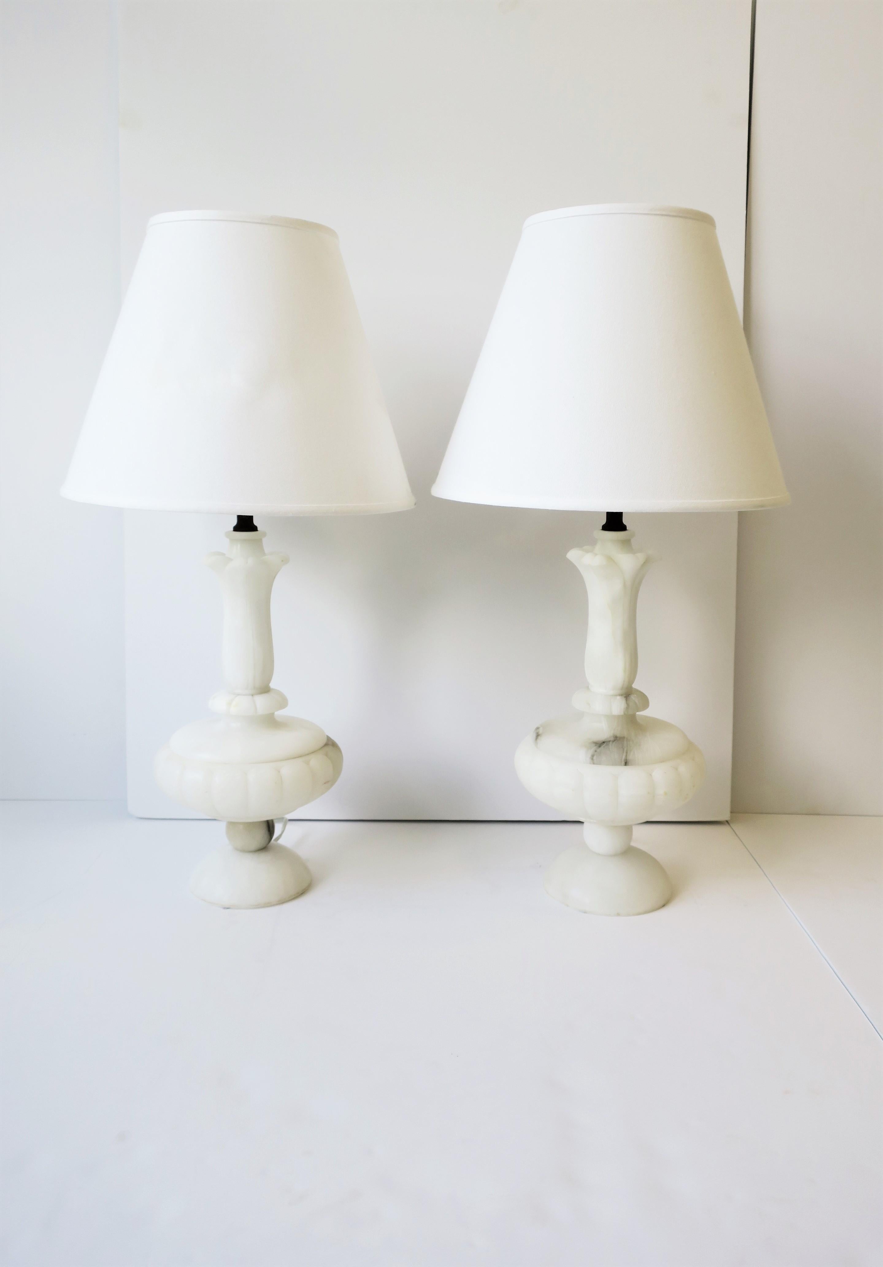 A beautiful and substantial pair of Italian white alabaster marble desk or table lamps in the neoclassical style, circa mid-20th century, Italy. Pair are predominantly white with some traces of dark gray veining. Carved detail at top neck and at