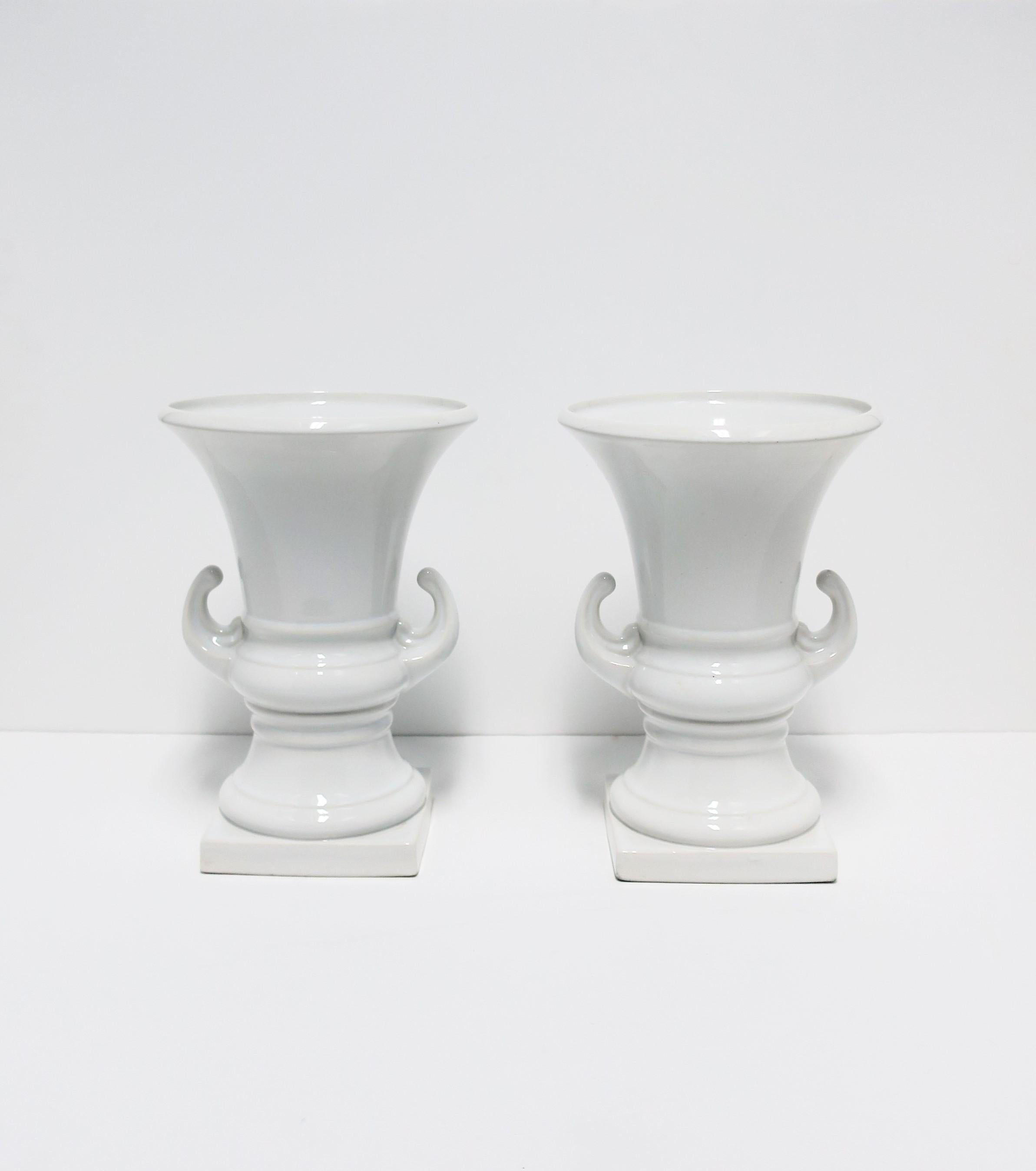 A pair of Italian white ceramic urns vases, Neoclassical style, circa late-20th century, Italy. Great as standalone pieces or as vases with flowers, etc. Urns are a nice height measuring 12