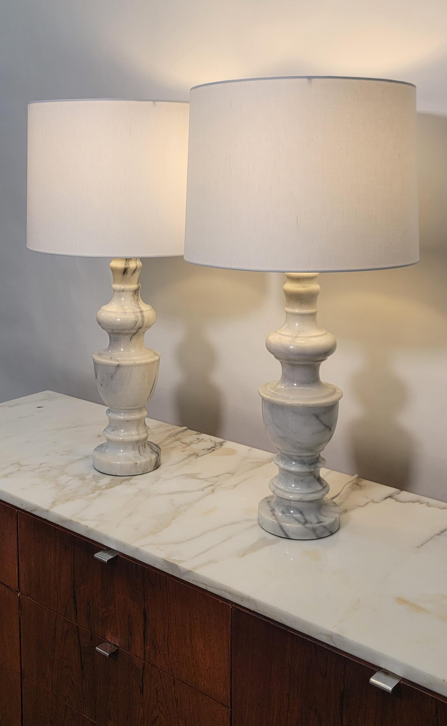 A beautiful and substantial pair of Italian white marble desk or table lamps in the Neoclassical style, circa 20th century, Italy. New white linen custom shades. Pair are predominantly white with some striking dark gray veining. A Classical urn lamp