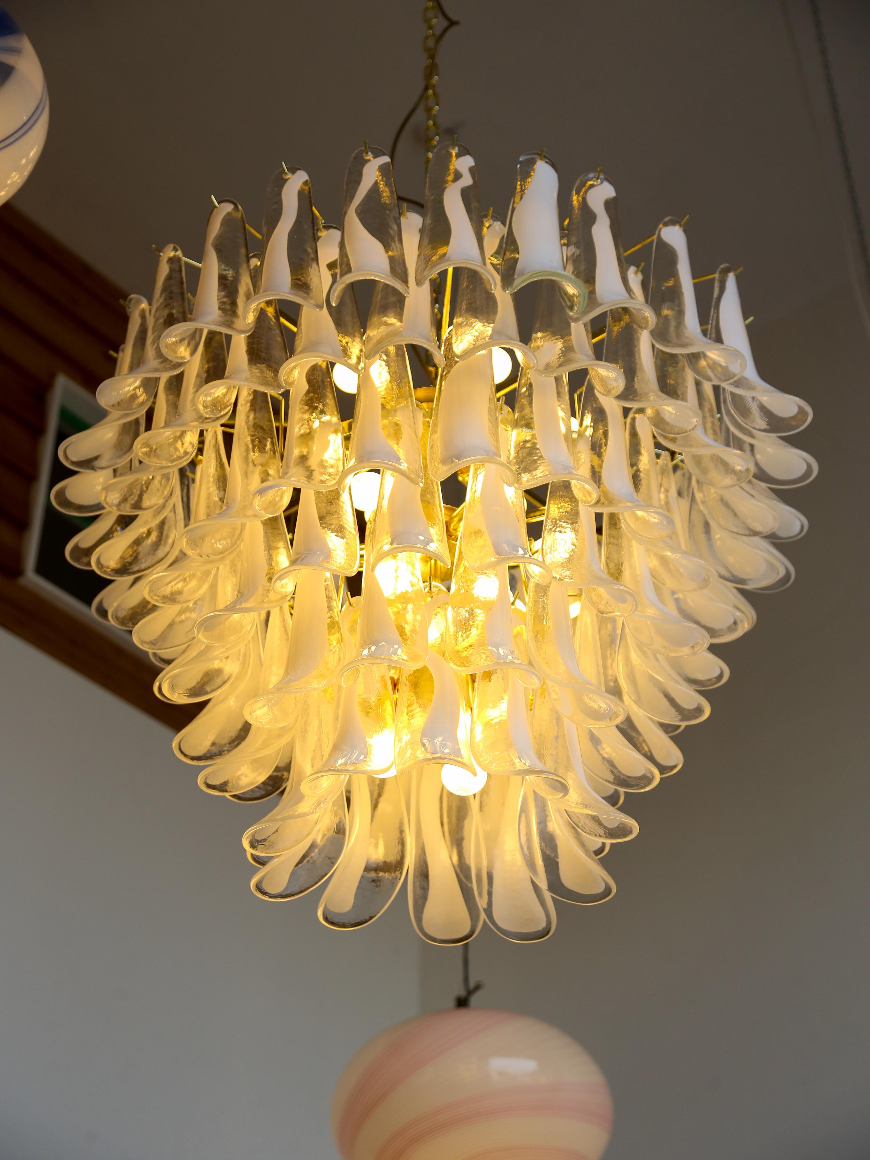 Statement piece in Murano white glass chandelier featuring a brass frame with six levels of saddles and eighteen internal light bulbs. ( total number of glass saddles is 103 )
This chandelier is a luxurious and elegant lighting fixture made but also