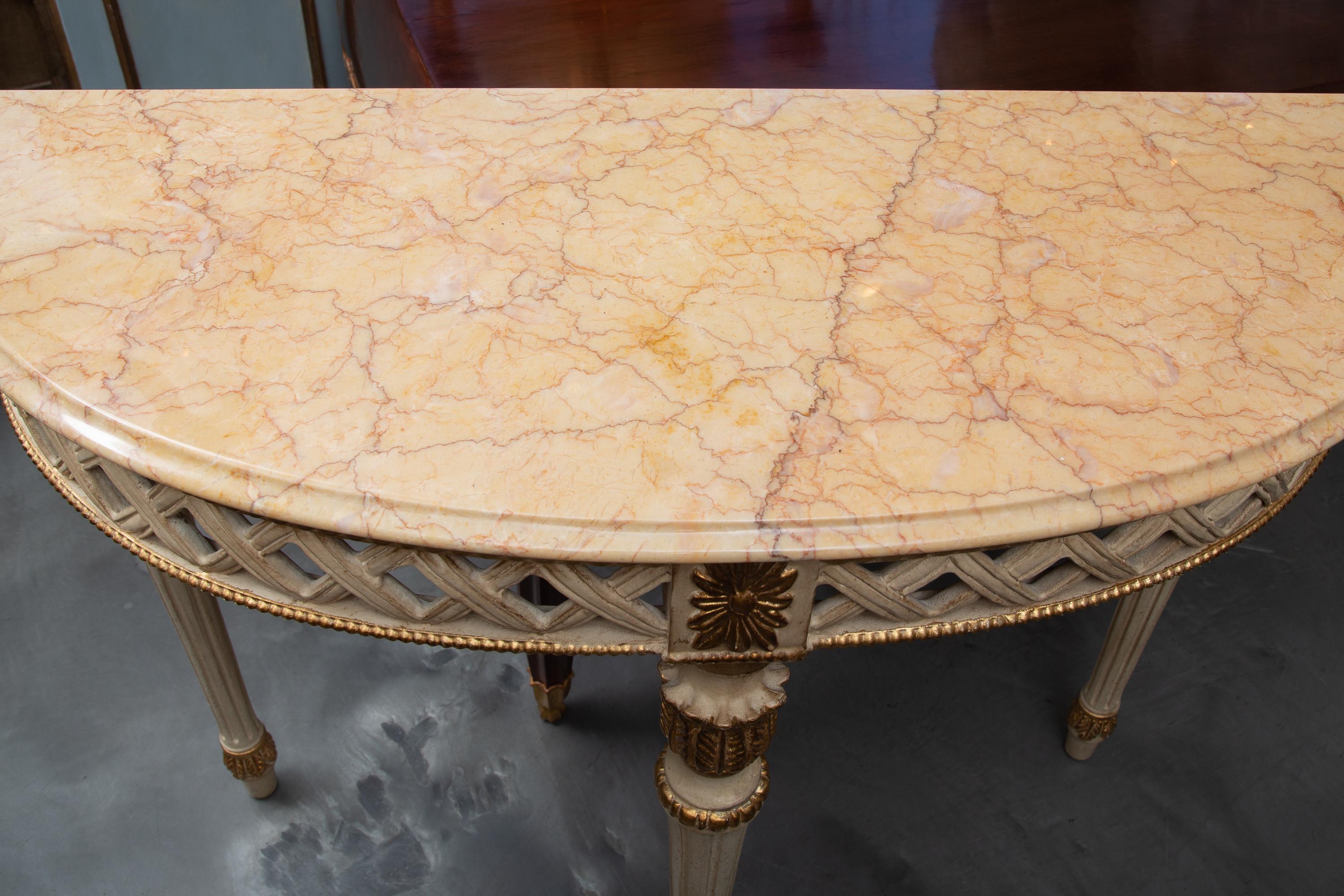This is a decorative Italian Louis XVI style white painted and parcel gilt demilune console, the sepia variegated marble top with molded edge over lattice-form frieze. The demilune console is supported by round tapering fluted legs. 20th century.