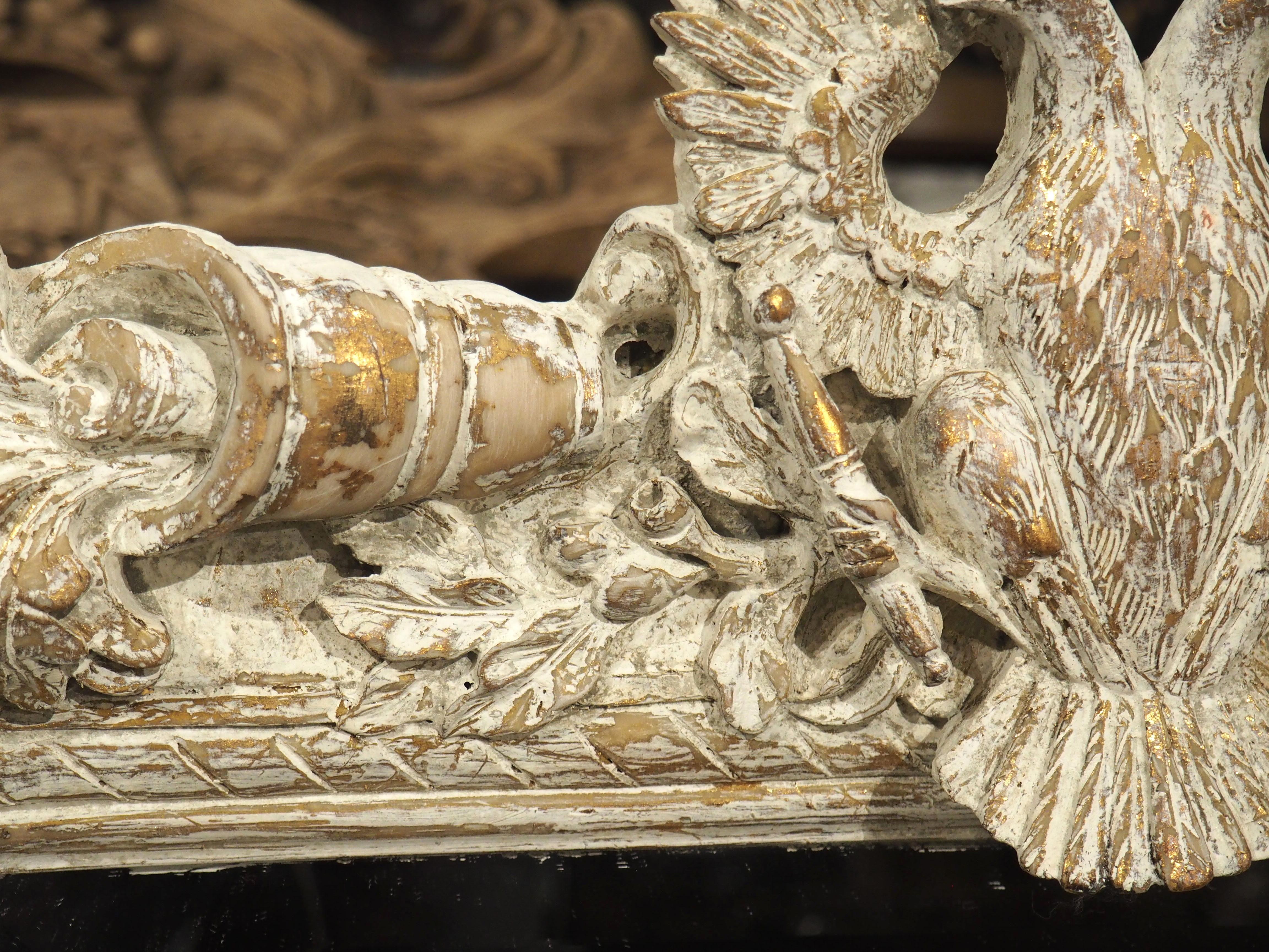 Ce miroir mural très décoratif est d'origine italienne et présente une finition blanche peinte en parcelles avec des accents légèrement dorés. Le verre biseauté est entouré d'une moulure de cannelures élancées légèrement interrompues en haut par un