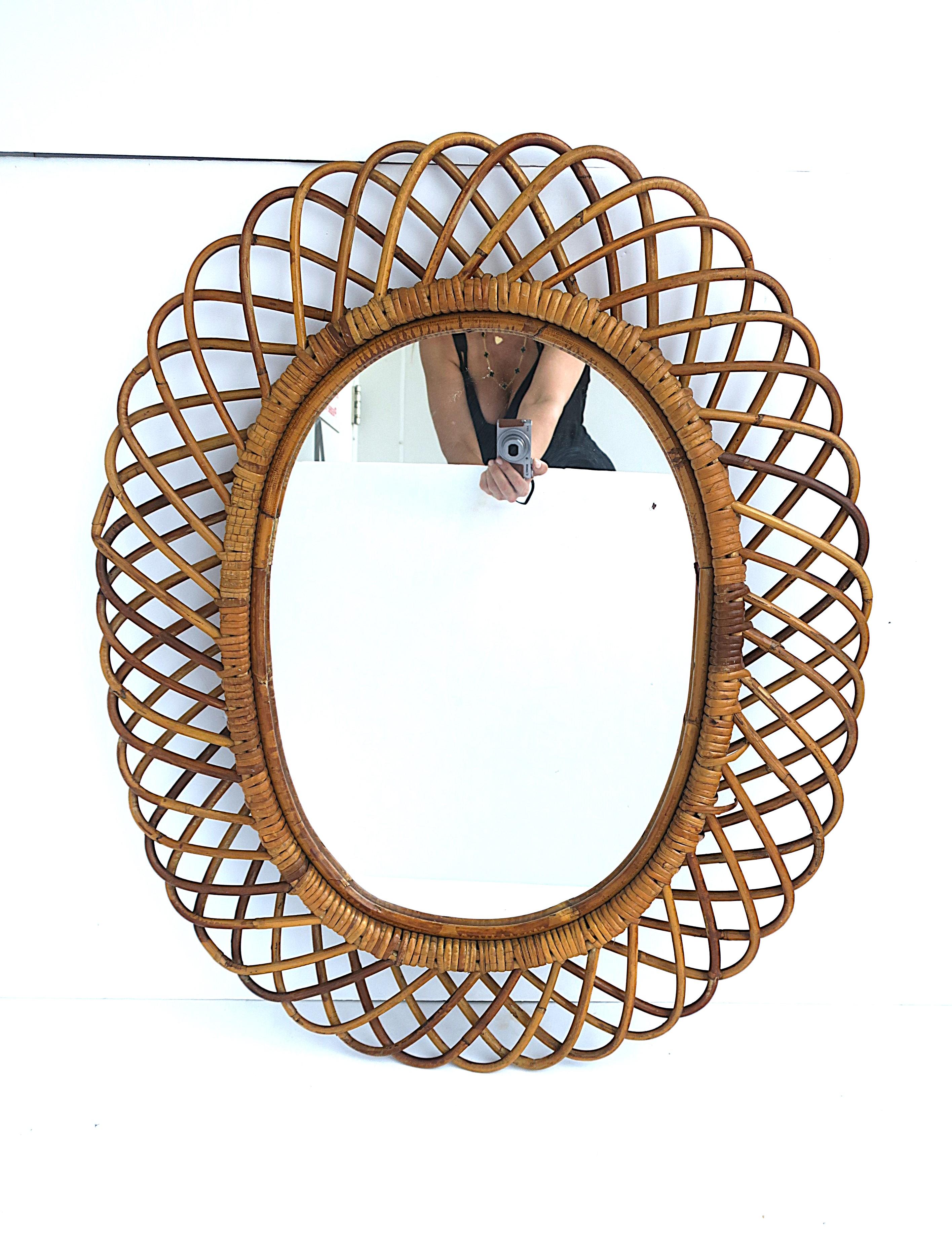 An Italian wicker rattan wall mirror in the style of designer, Franco Albini, by Rosenthal-Netter, circa mid-20th century, Italy. Mirror is oval with a wicker latticework frame. A great piece for a foyer/hall, vanity, bath/powder room, etc. Mirror