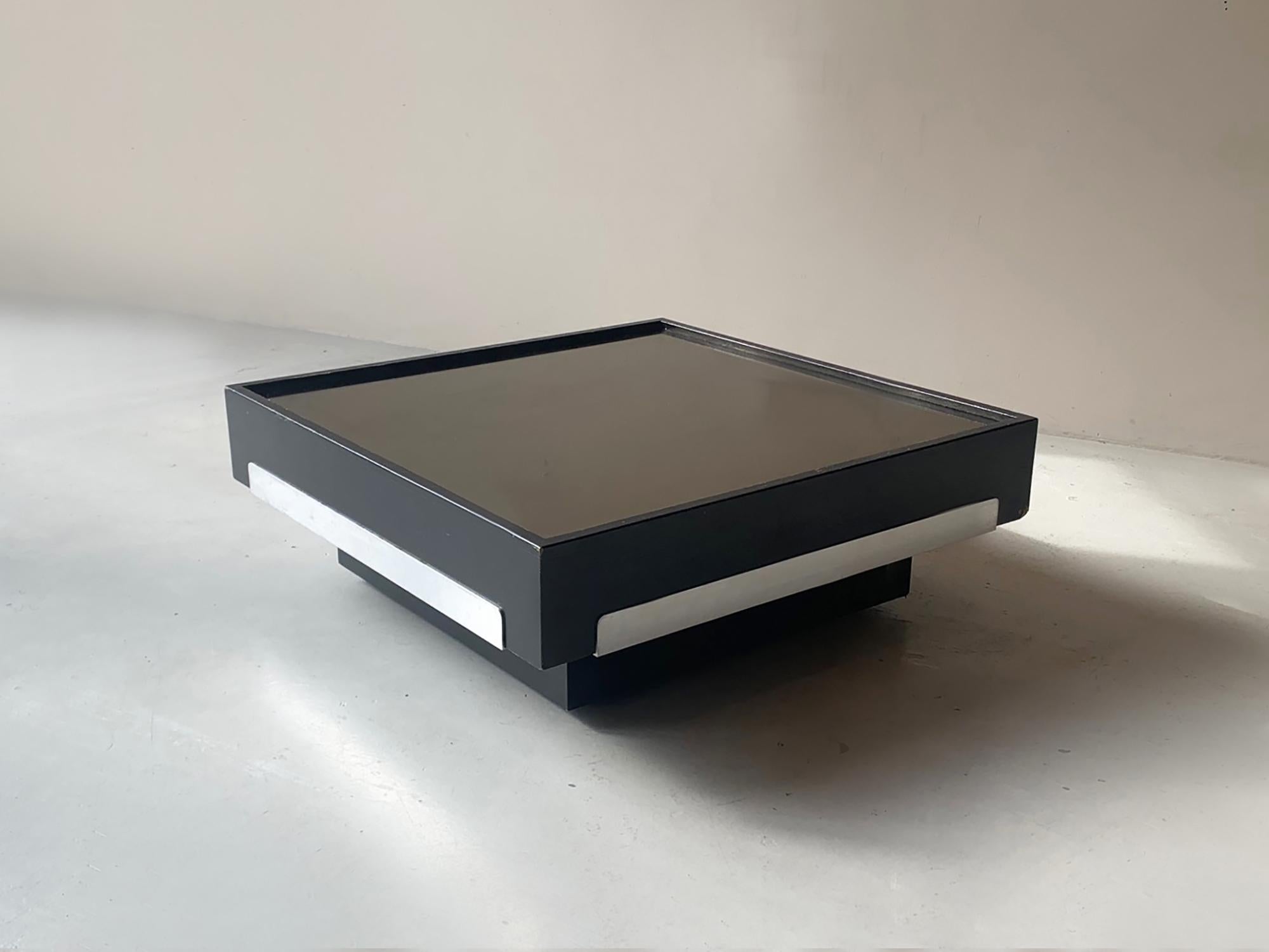 Square Mid-Century Modern coffee table made in Italy in the 1970s which is similar to the designs of Willy Rizzo. Mirrored table top which has a very subtle peach coloured tint. Black ash sides with metal strips. Sits on totally hidden castors so