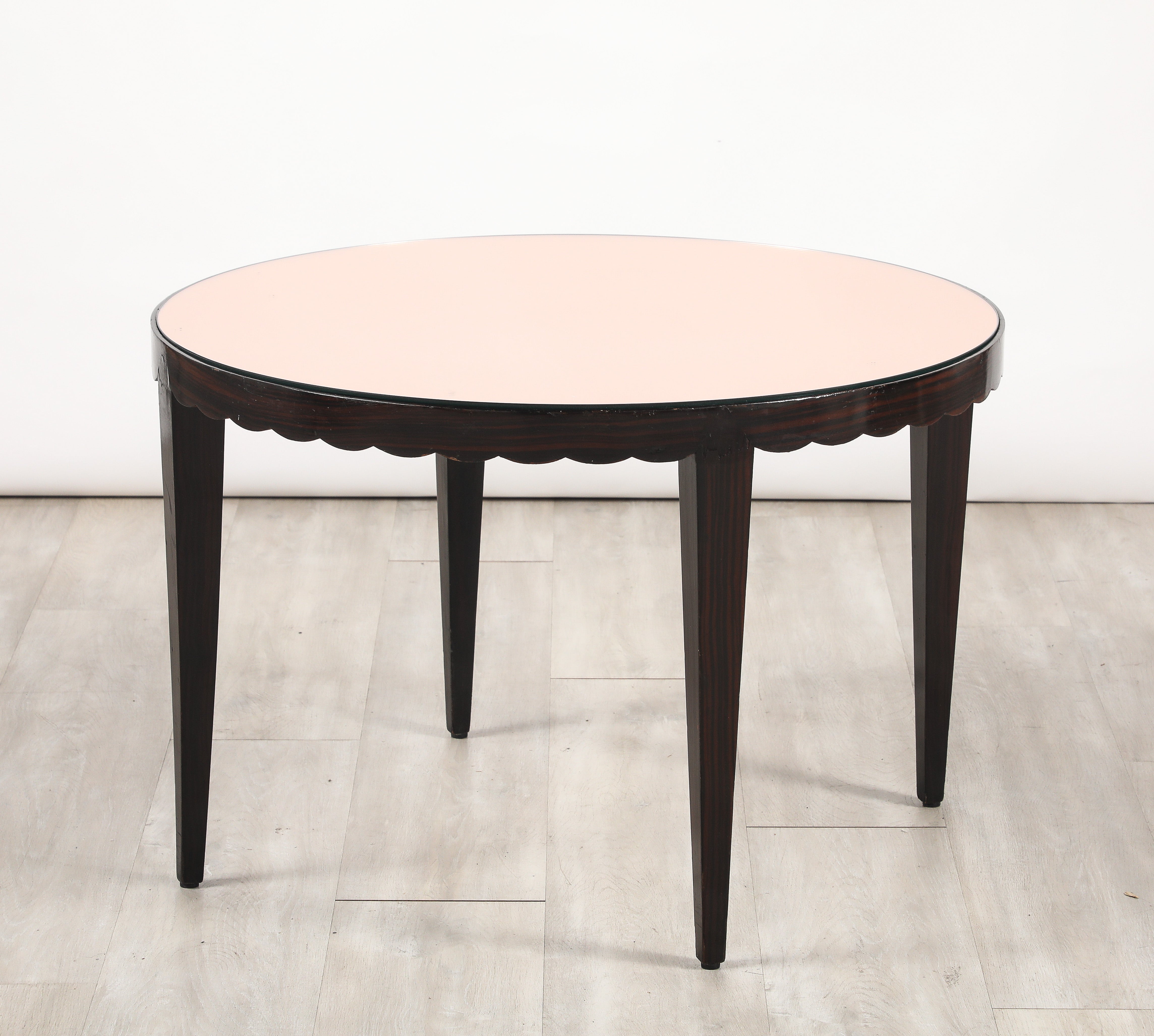 Table de cocktail circulaire italienne en ébène de Macassar avec un plateau en verre incrusté d'or rose, soutenu par un tablier festonné sur des pieds élégamment fuselés.  Une pièce raffinée et unique. 
Italie du Nord, vers 1950 
