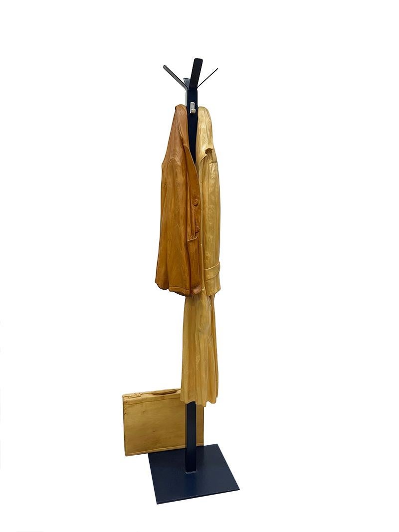 Italian wood-carved sculptures with raincoat and jacket on metal coat rack

Italian hand-carved wooden sculptures hanging on the coat rack and a suitcase standing next to the coat rack. The wooden coats hang loose on the hook of the coat rack with