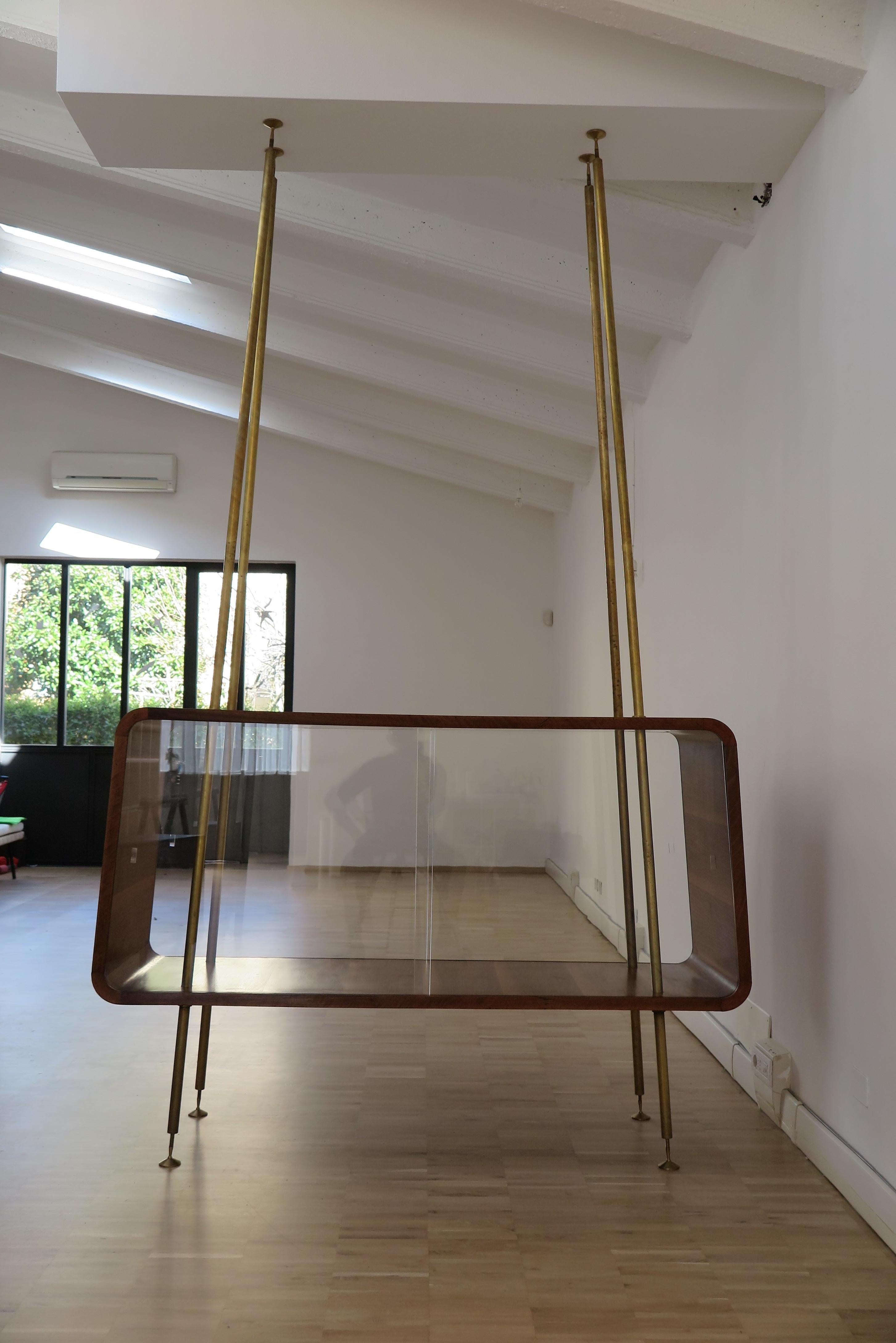 Amazing and fabulous Italian display cabinet or buffets or room separator with sliding glass doors with brass circular section adjustable uprights fixed to the floor and ceiling, the wooden furniture is in the shape of a trapezium with rounded